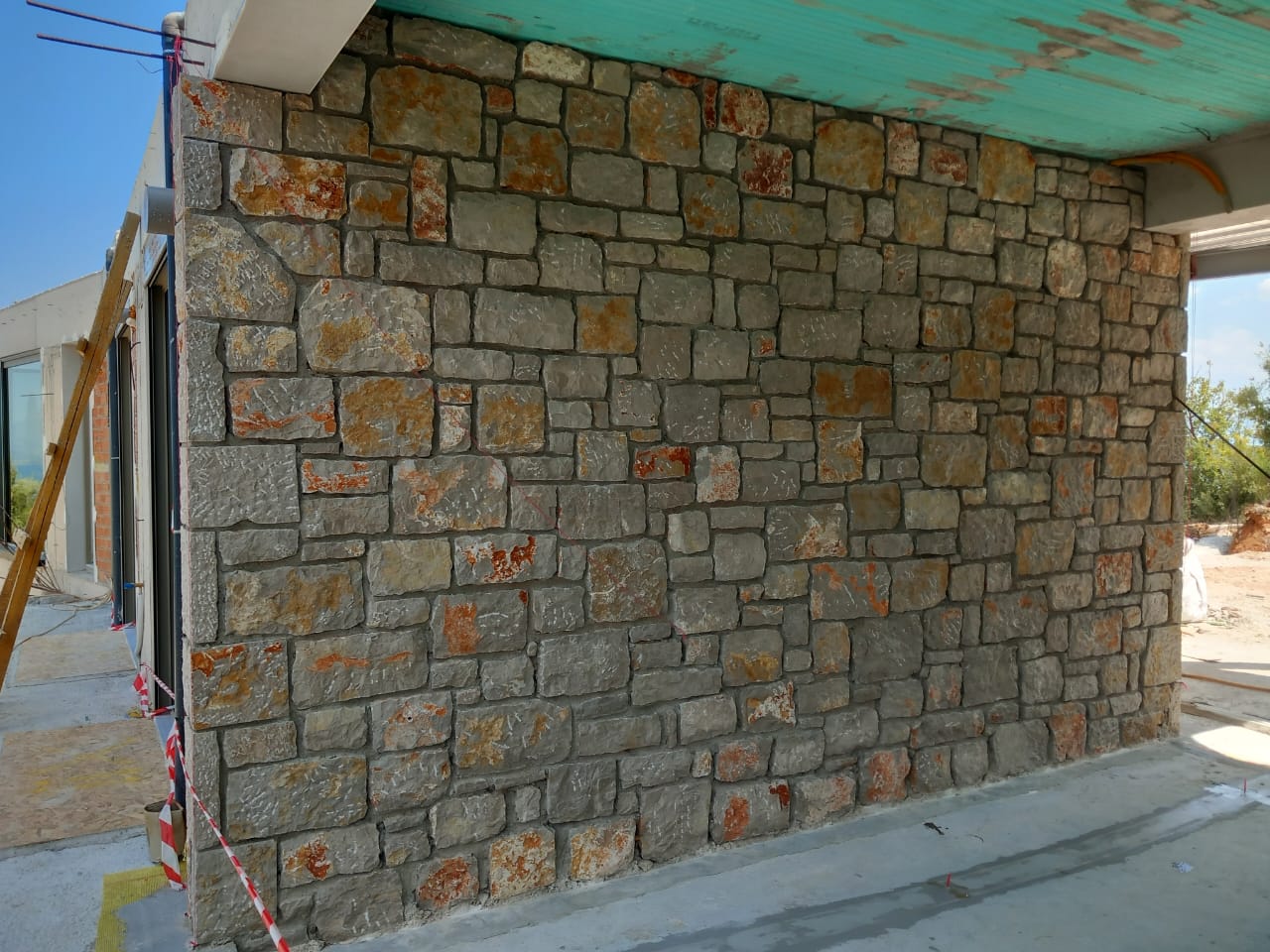 Stone wall with irregularly shaped stones, some with reddish hues, under a greenish roof extension.