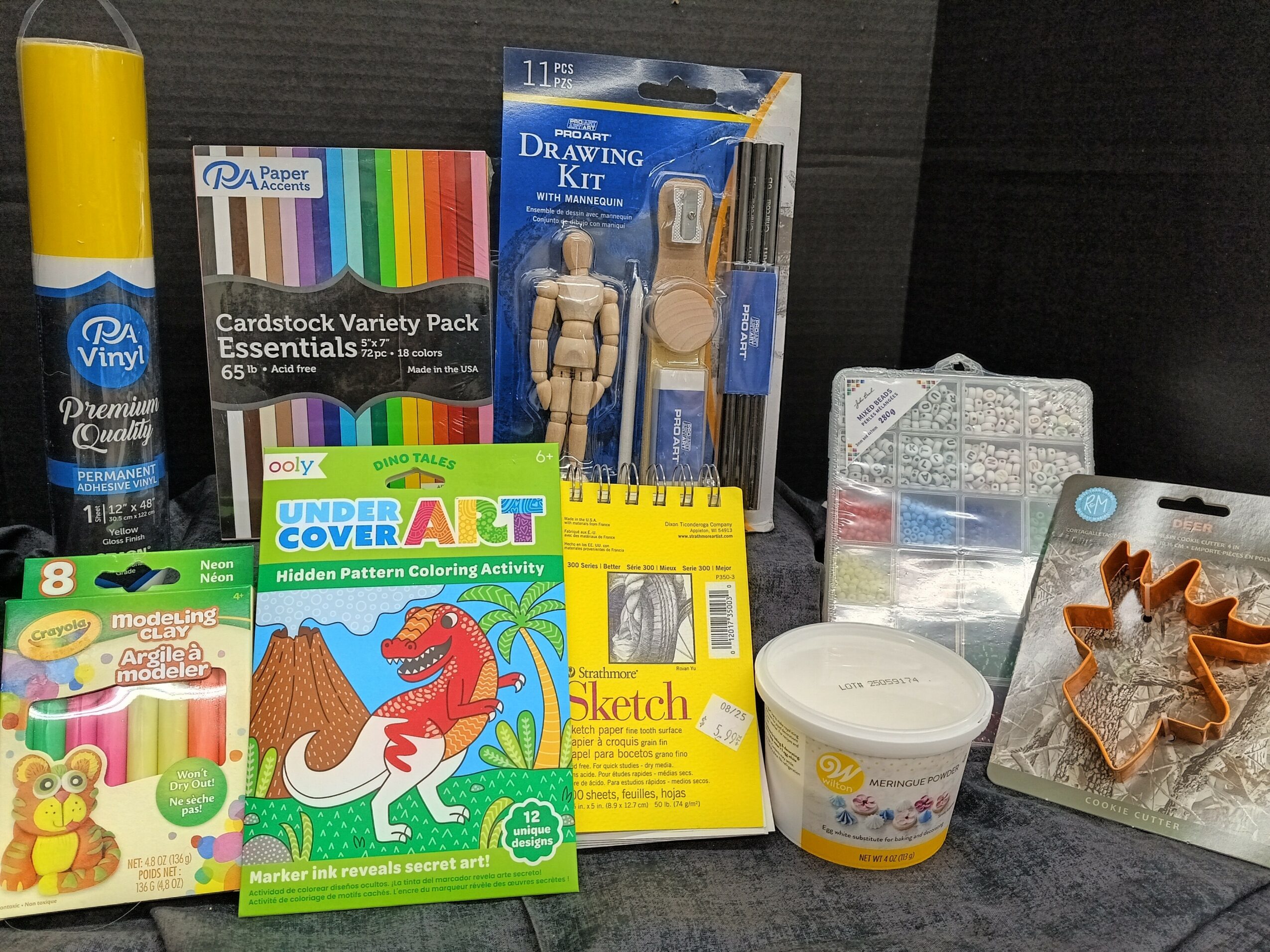 Assorted arts and crafts supplies including markers, a drawing kit, modeling clay, coloring activity book, and decorative items on a table.