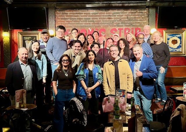 Group of people posing together in a restaurant or bar setting with brick wall background.
