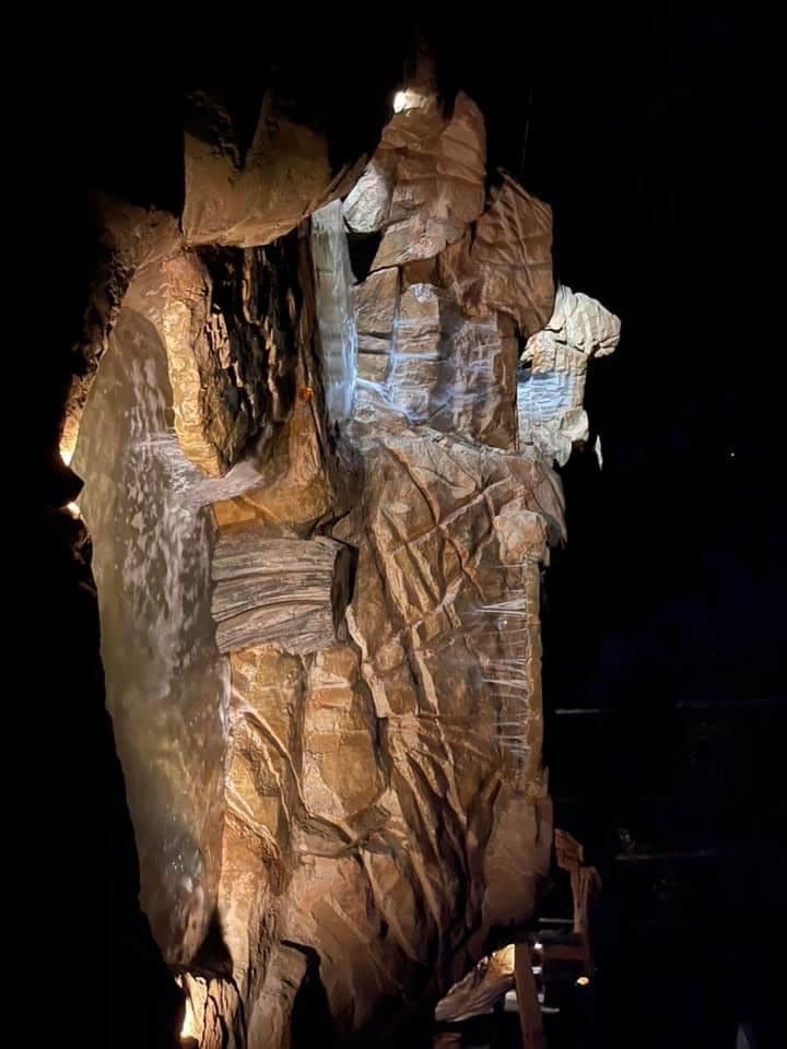 Rock formation illuminated at night with dark sky background, showing layered textures and colors.