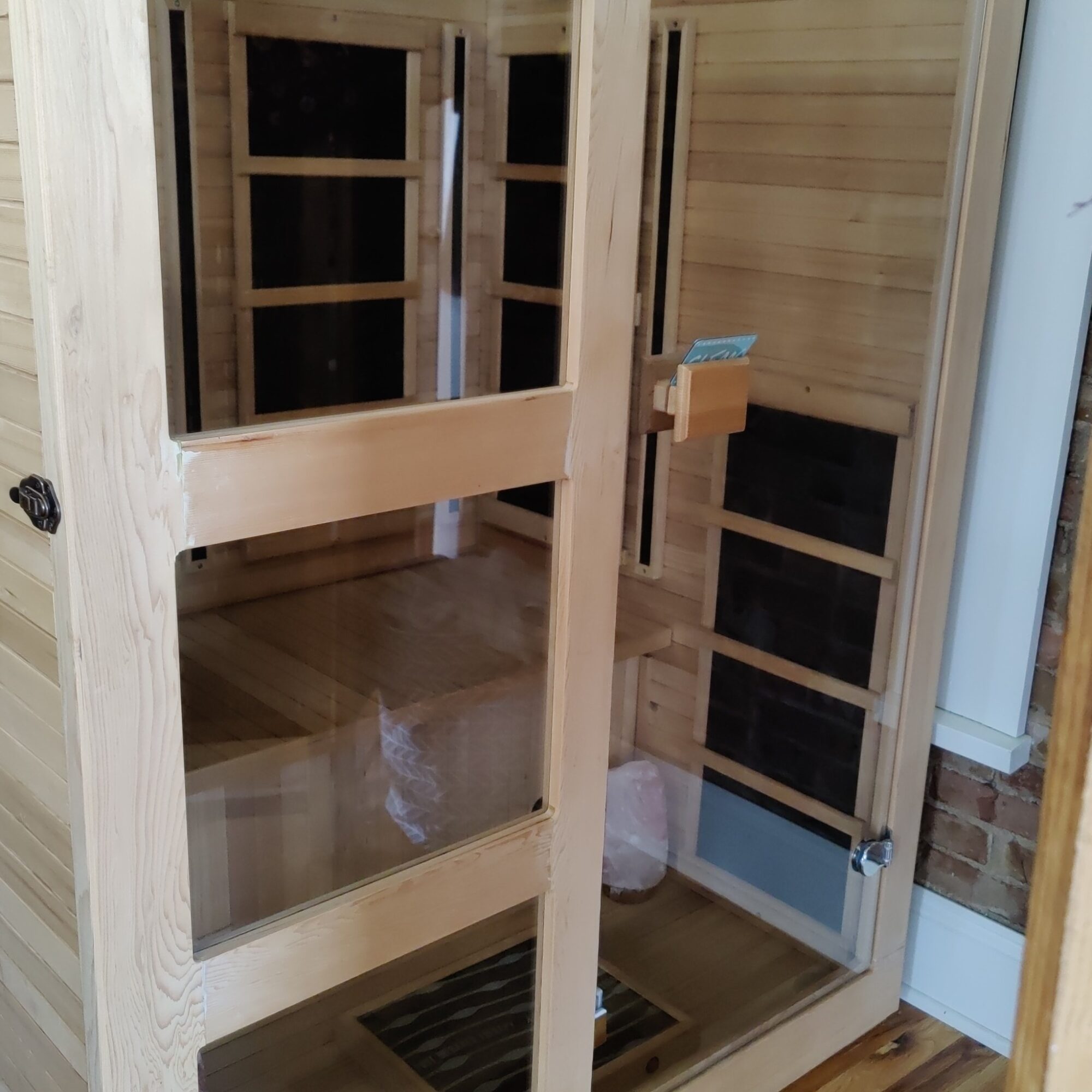 Interior of a wooden sauna with benches, a heater, and a window, showing light-colored wood paneling.