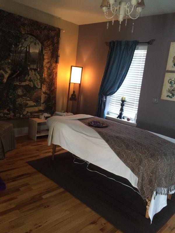 Room with bed, window with blue curtain, tapestry on wall, lamp, chandelier, and wooden floor.