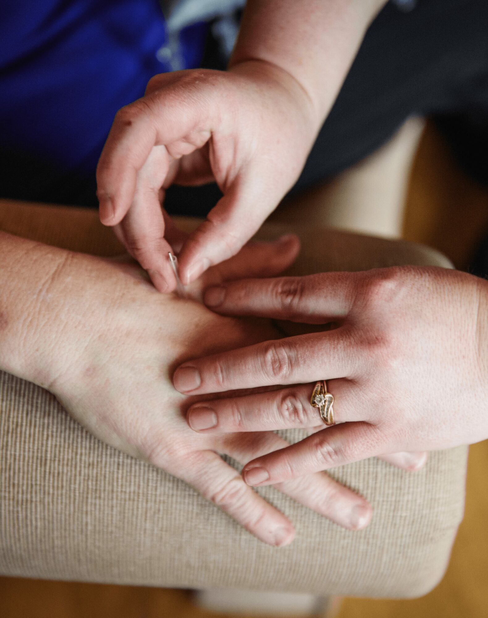Multiple hands gently holding each other, one with a ring, on a beige surface.