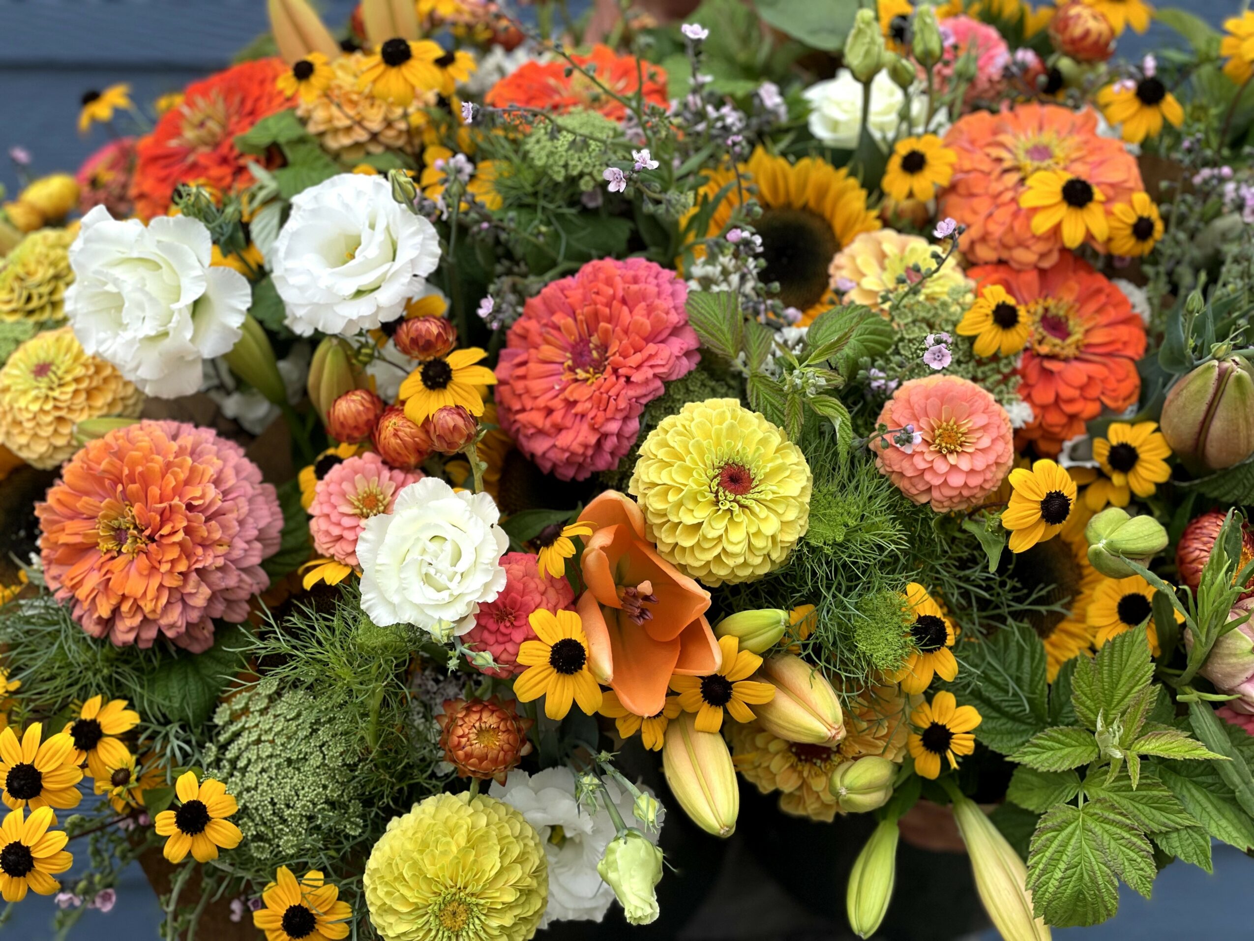 Colorful bouquet of various flowers including sunflowers, roses, and marigolds with green leaves.