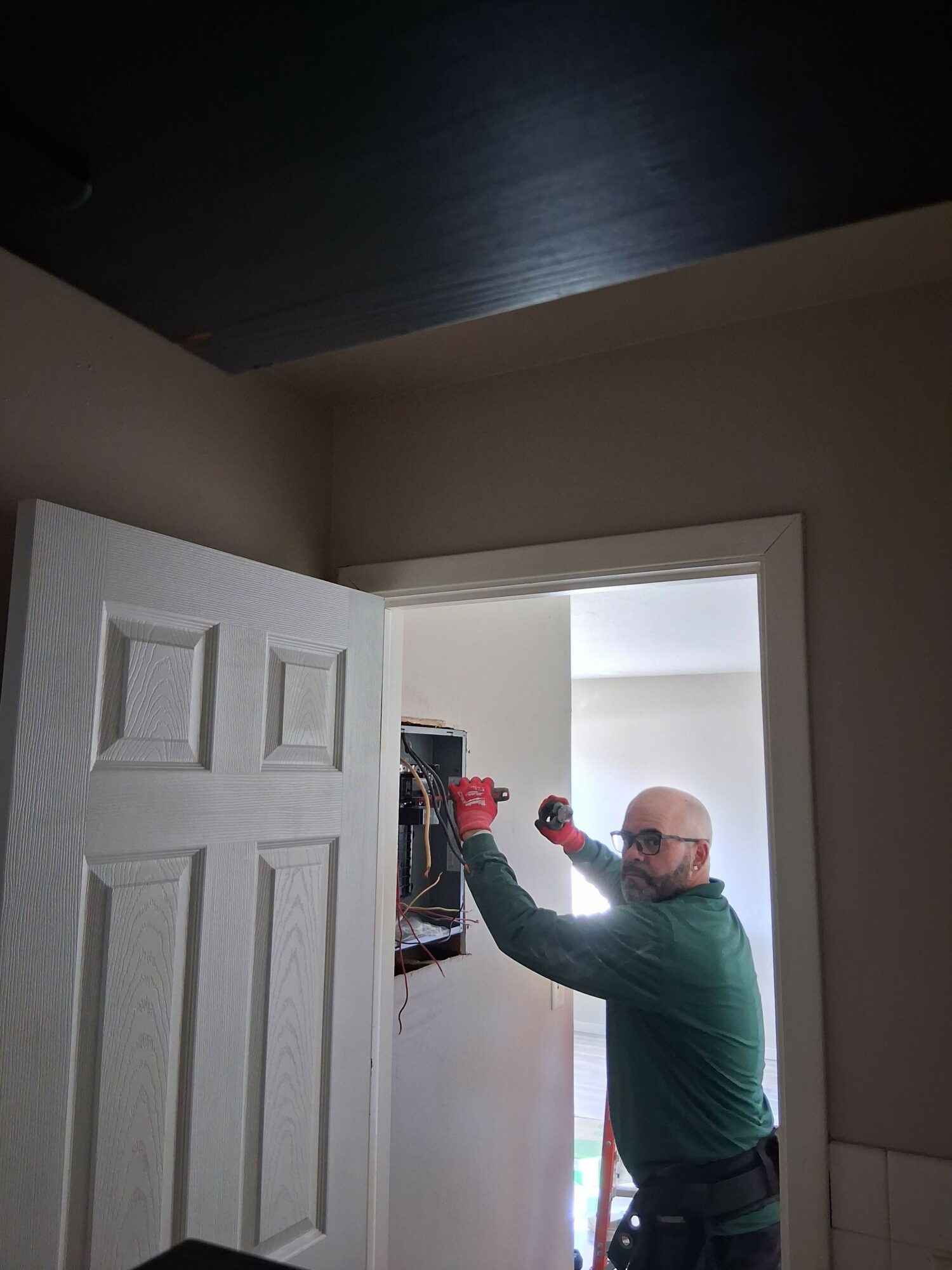 Person with glasses and green jacket reaching into a closet with shelves and clothes.