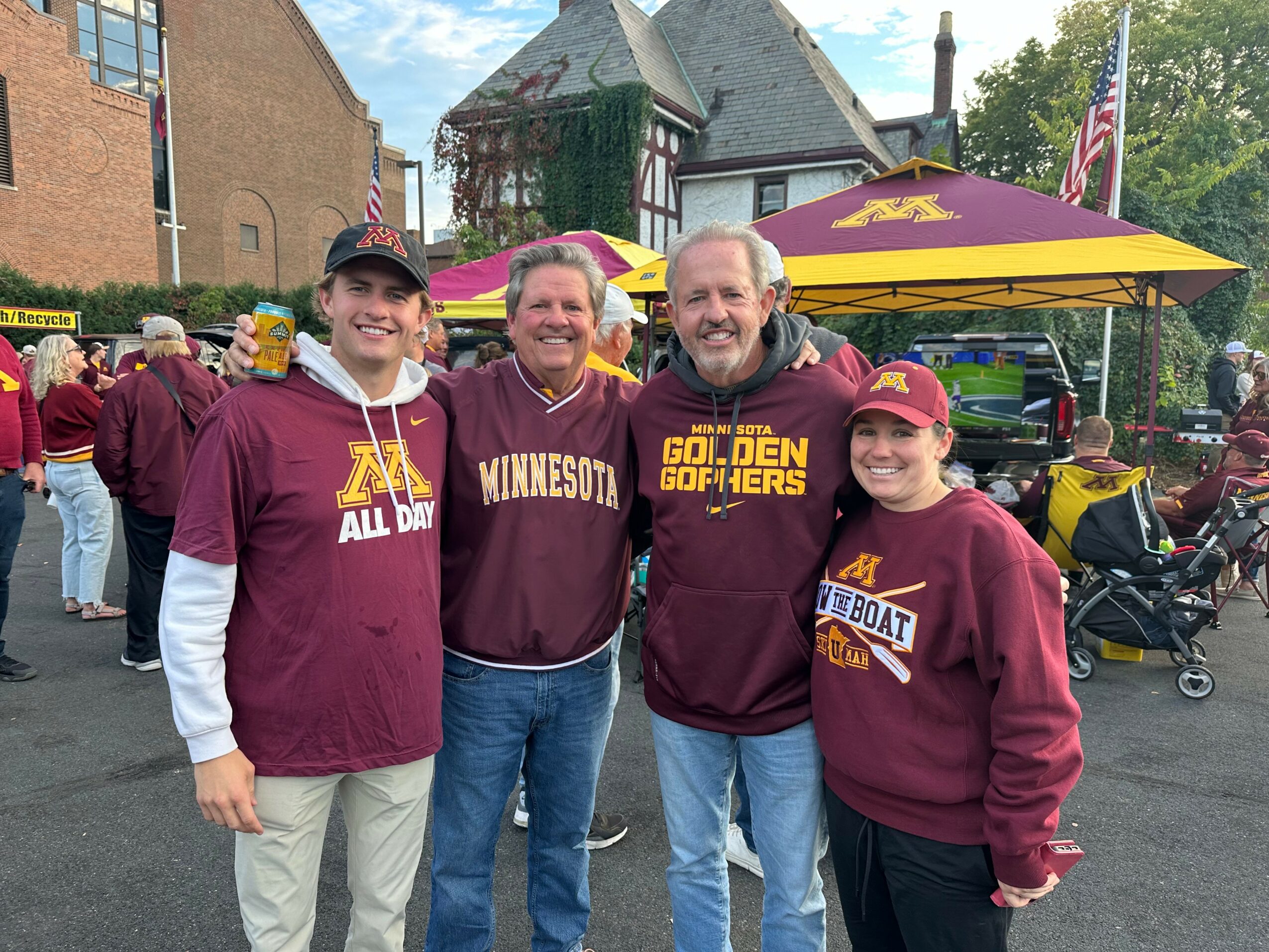 Four people wearing Minnesota Golden Gophers apparel standing outdoors at a tailgate event, smiling.
