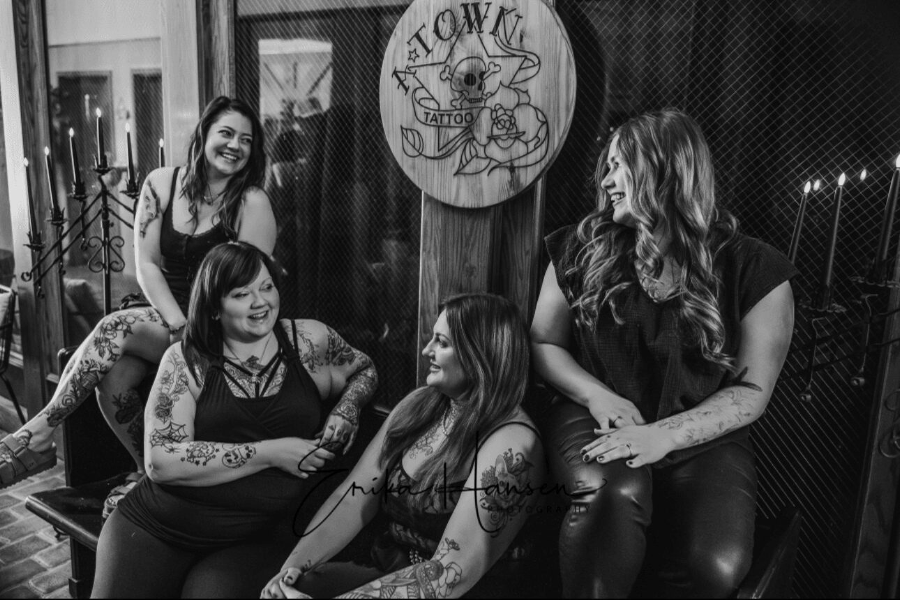 Four women sitting and standing together in a room, smiling and talking, with a circular sign on the wall behind them.