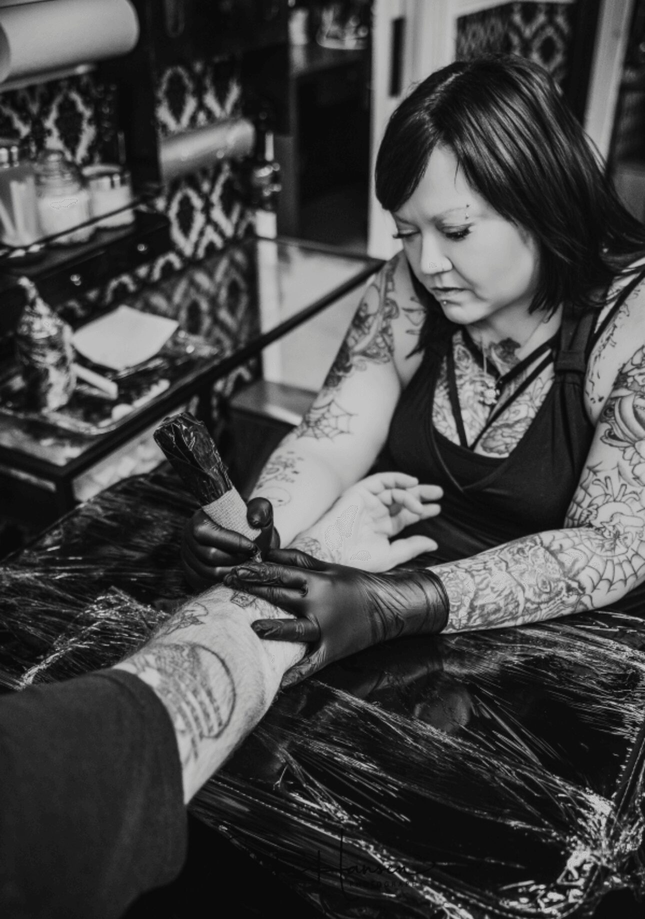 Tattoo artist applying tattoo to person's arm in a studio with tattoo supplies on shelves.