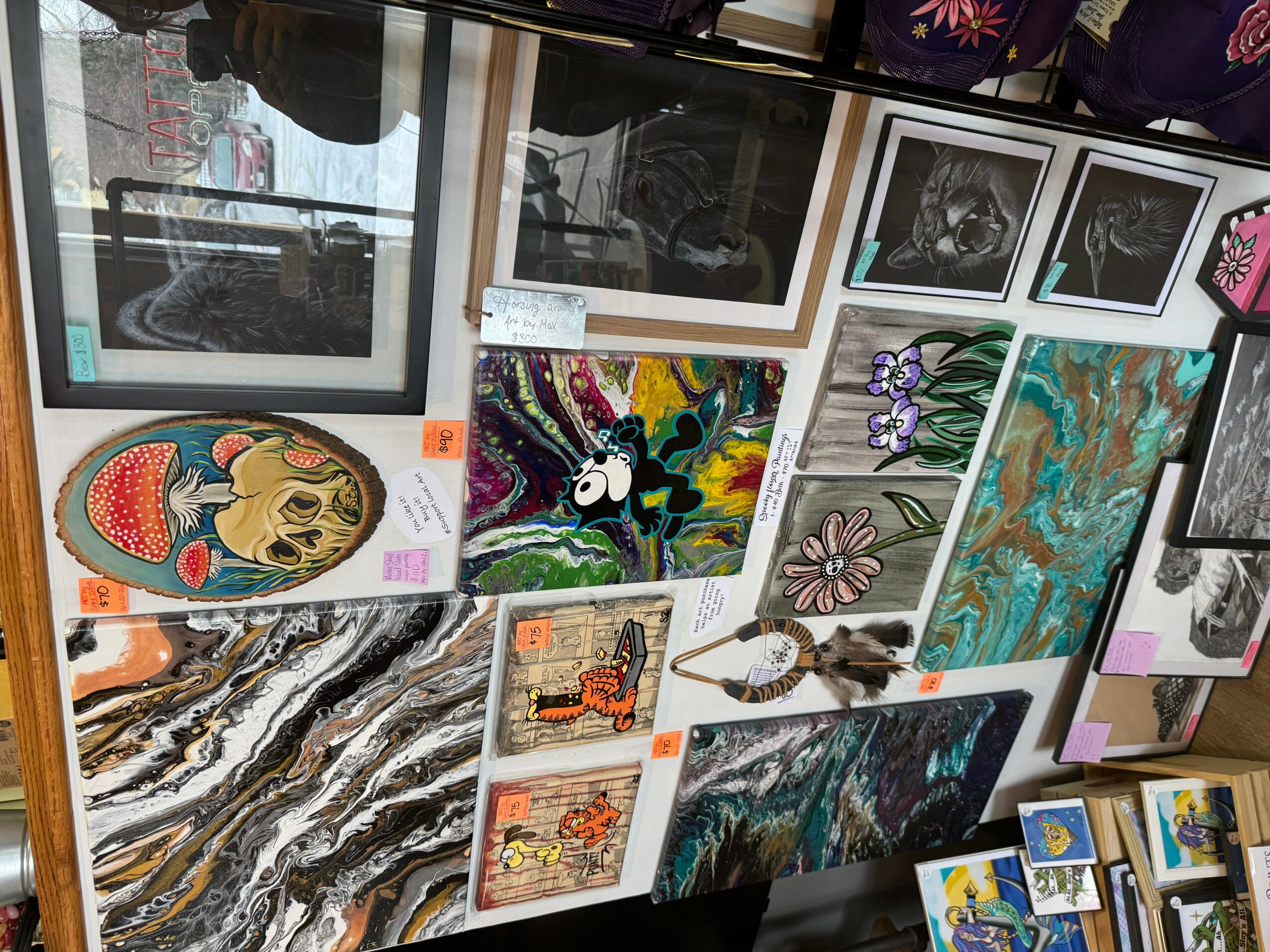 Gallery wall with various colorful paintings and photographs, including abstract, floral, and animal images, displayed on a white wall.