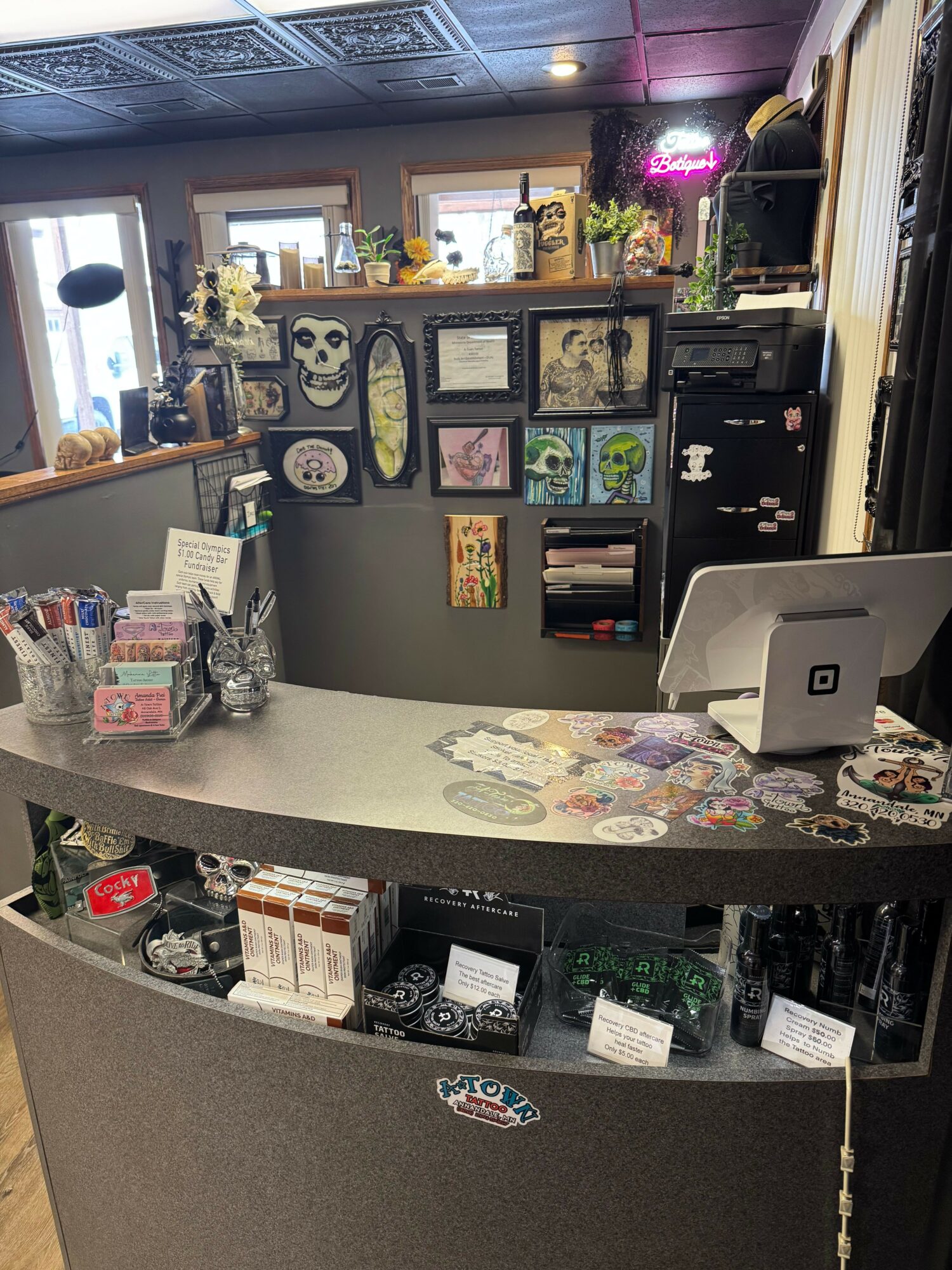 Counter with various items, including a computer, pens, and decorative objects, in a room with artwork and shelves in the background.
