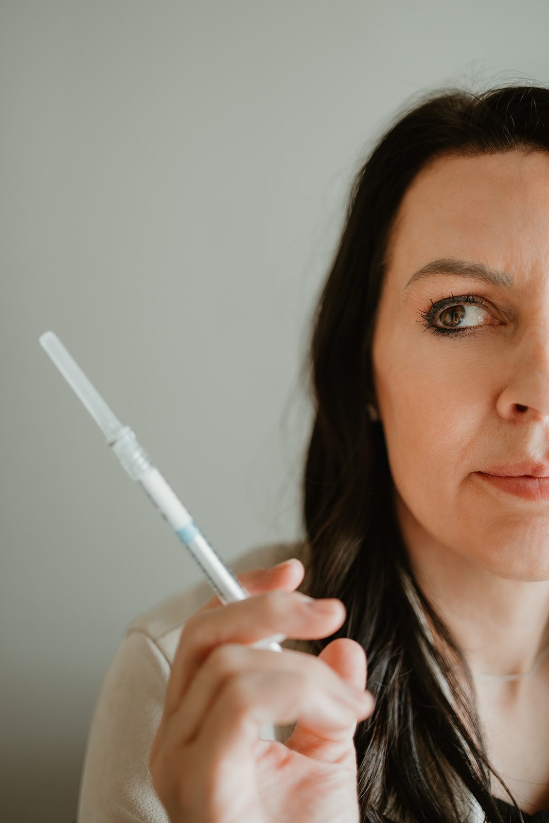Woman holding a syringe, with only part of her face visible, against a plain background.