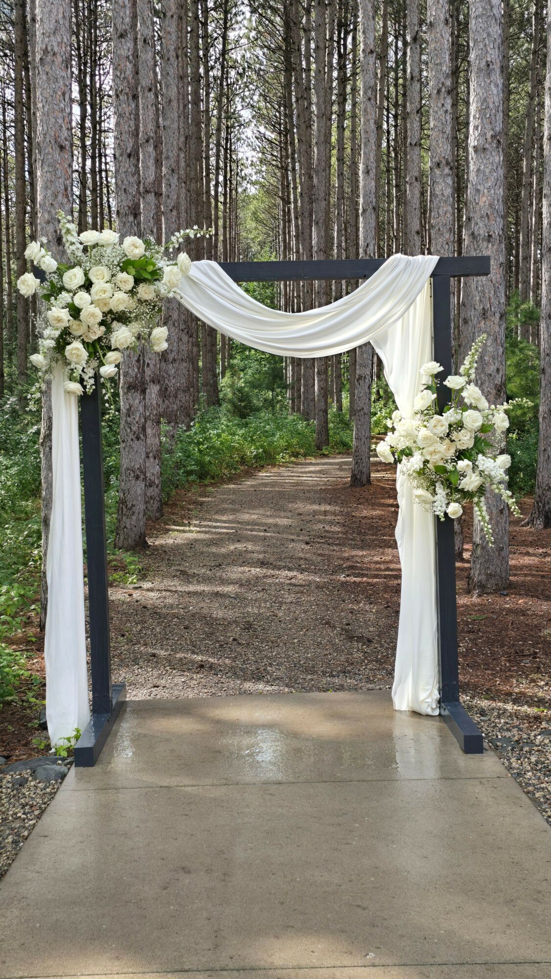 Wedding arch decorated with white flowers and fabric in a forest setting.