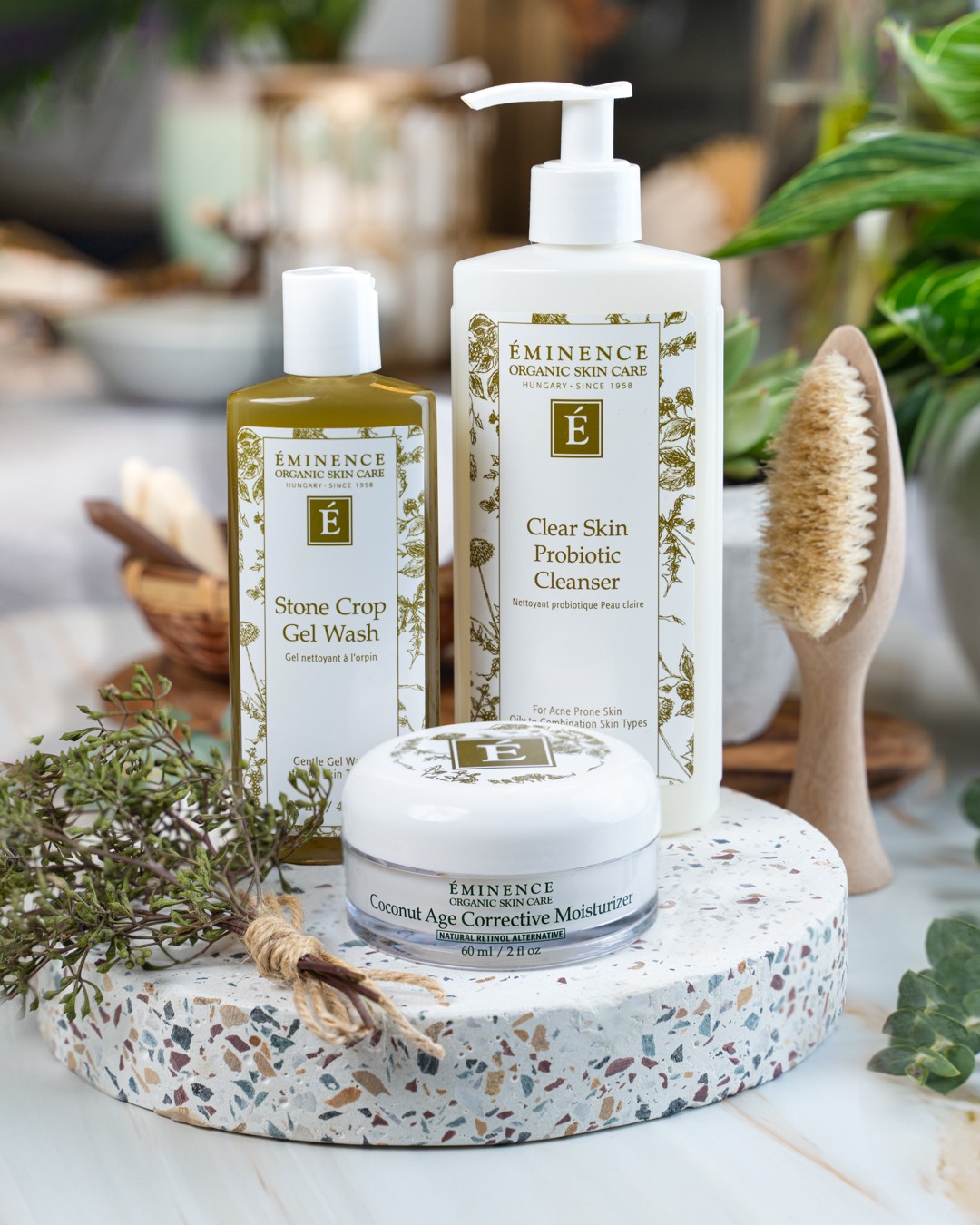 Three skincare products on a terrazzo surface with a plant and wooden brush in the background.