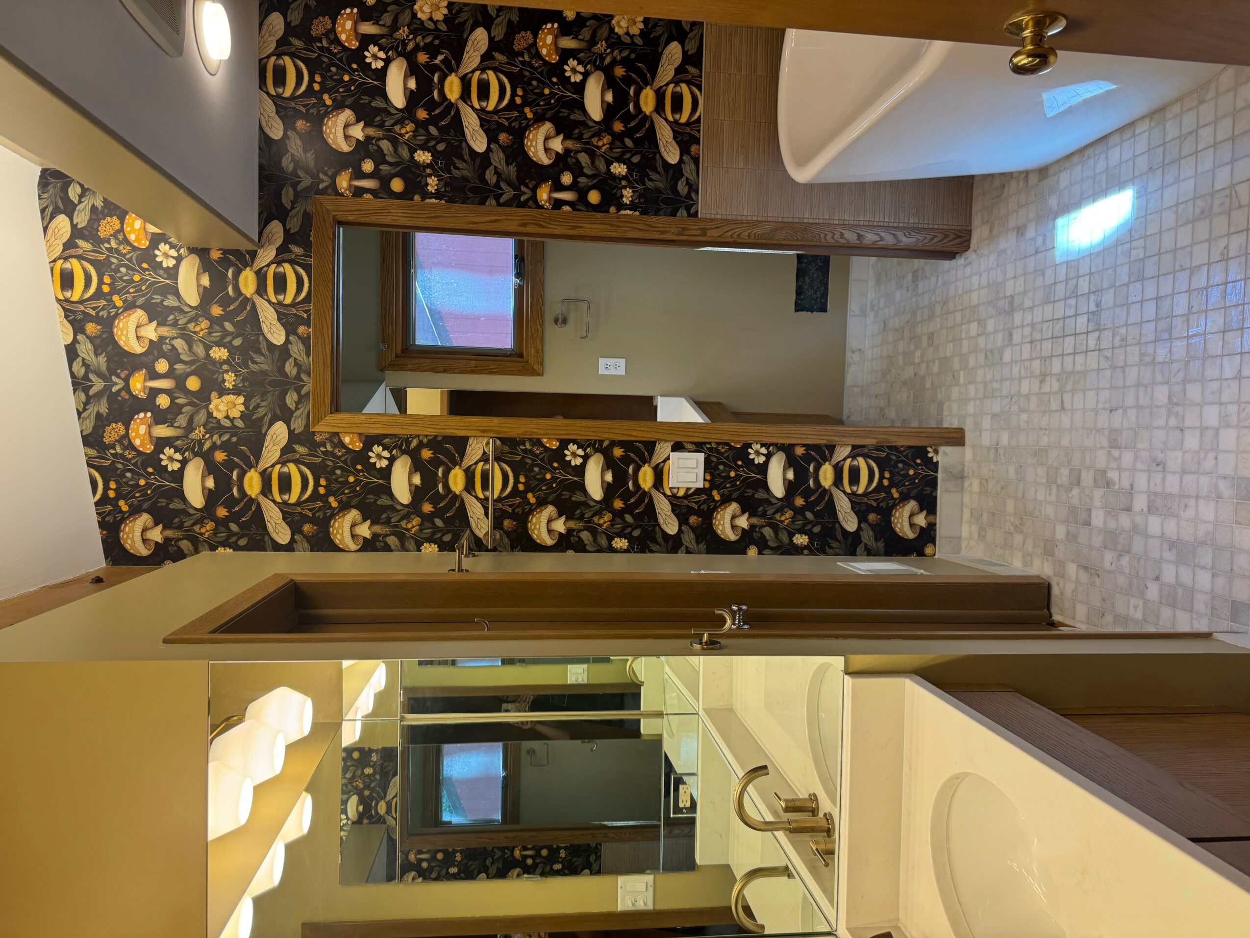 Bathroom with a mirror, sink, and patterned wallpaper, visible through an open door, with tiled floor and a window.