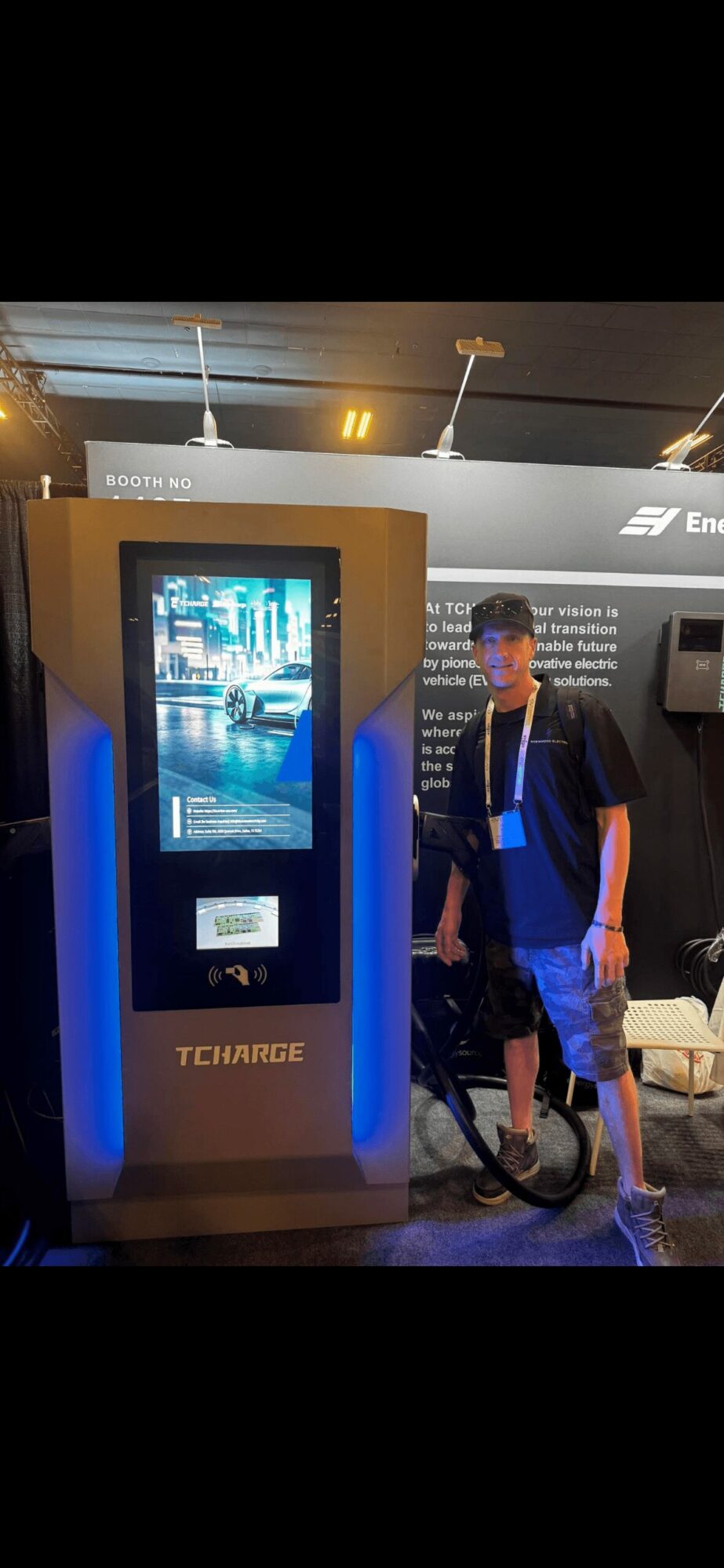 Person standing next to a tall, illuminated kiosk with a screen displaying a city scene at night.