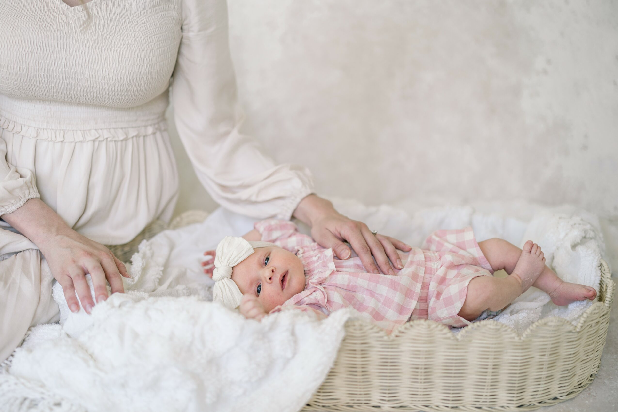 Baby lying in a woven basket on a soft blanket, with an adult's hand gently touching the baby.