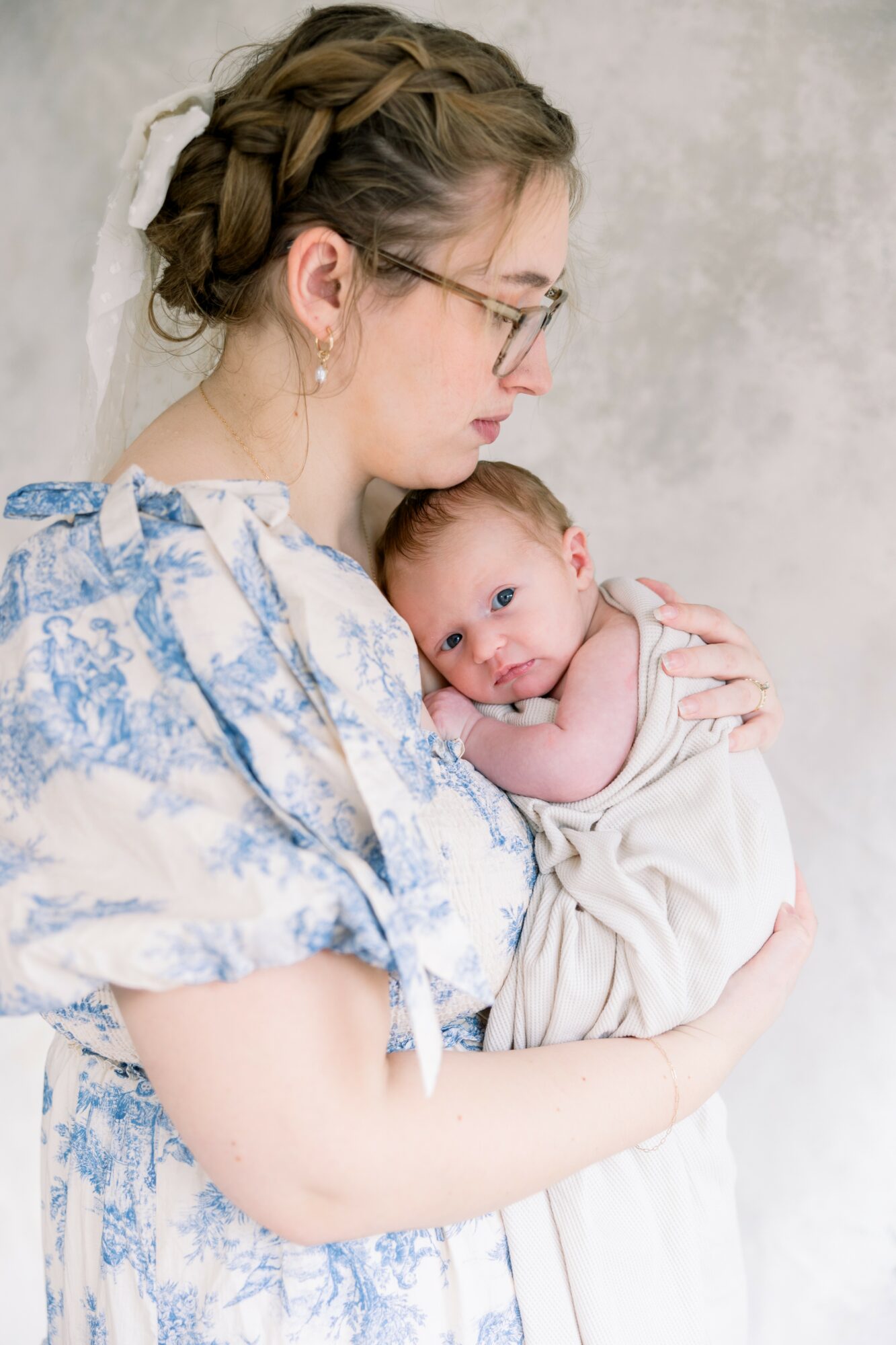 Woman holding a baby close, both looking to the side, against a plain background.