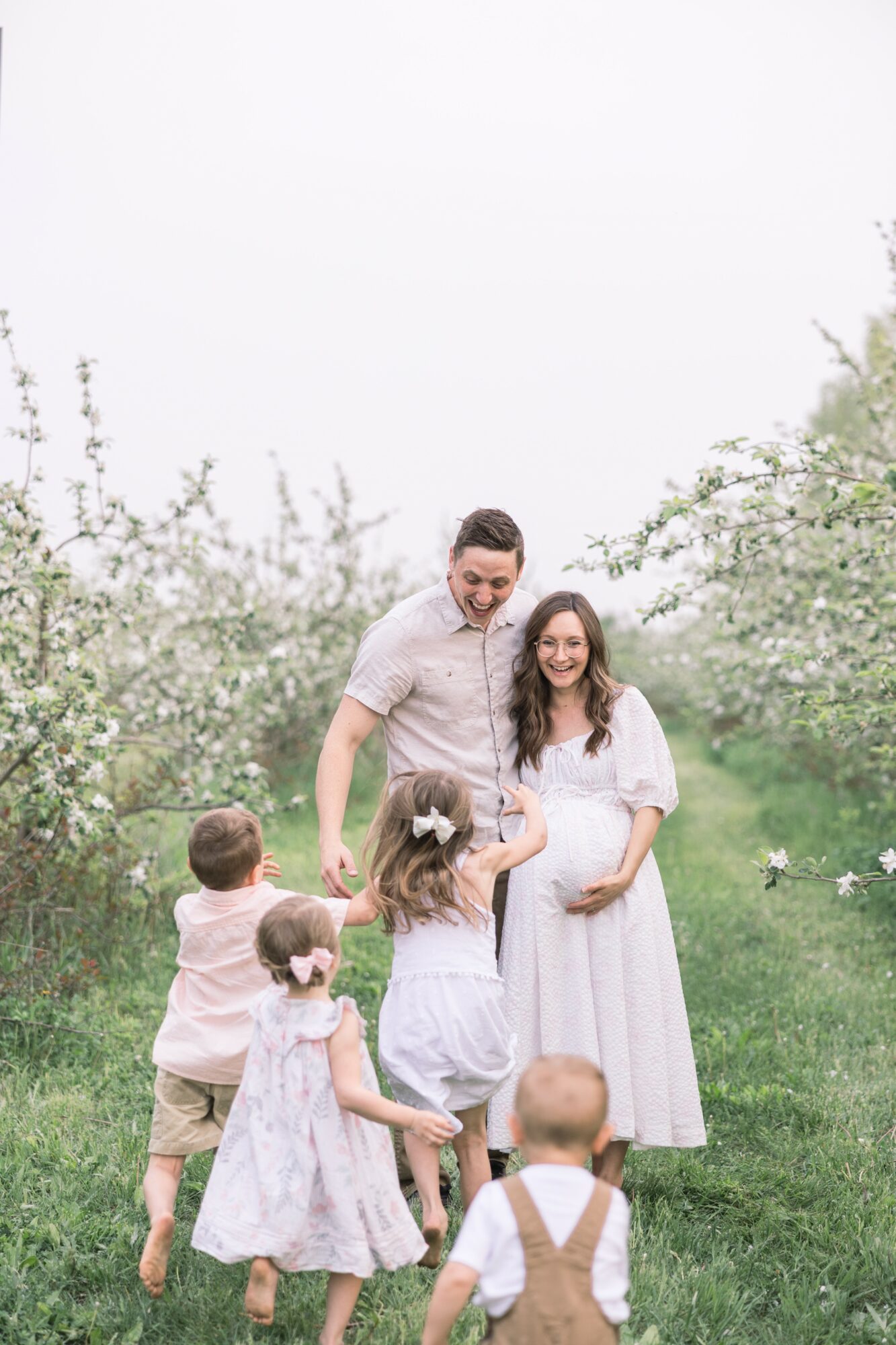 Family of six standing outdoors on a grassy path with blooming trees, smiling and interacting.