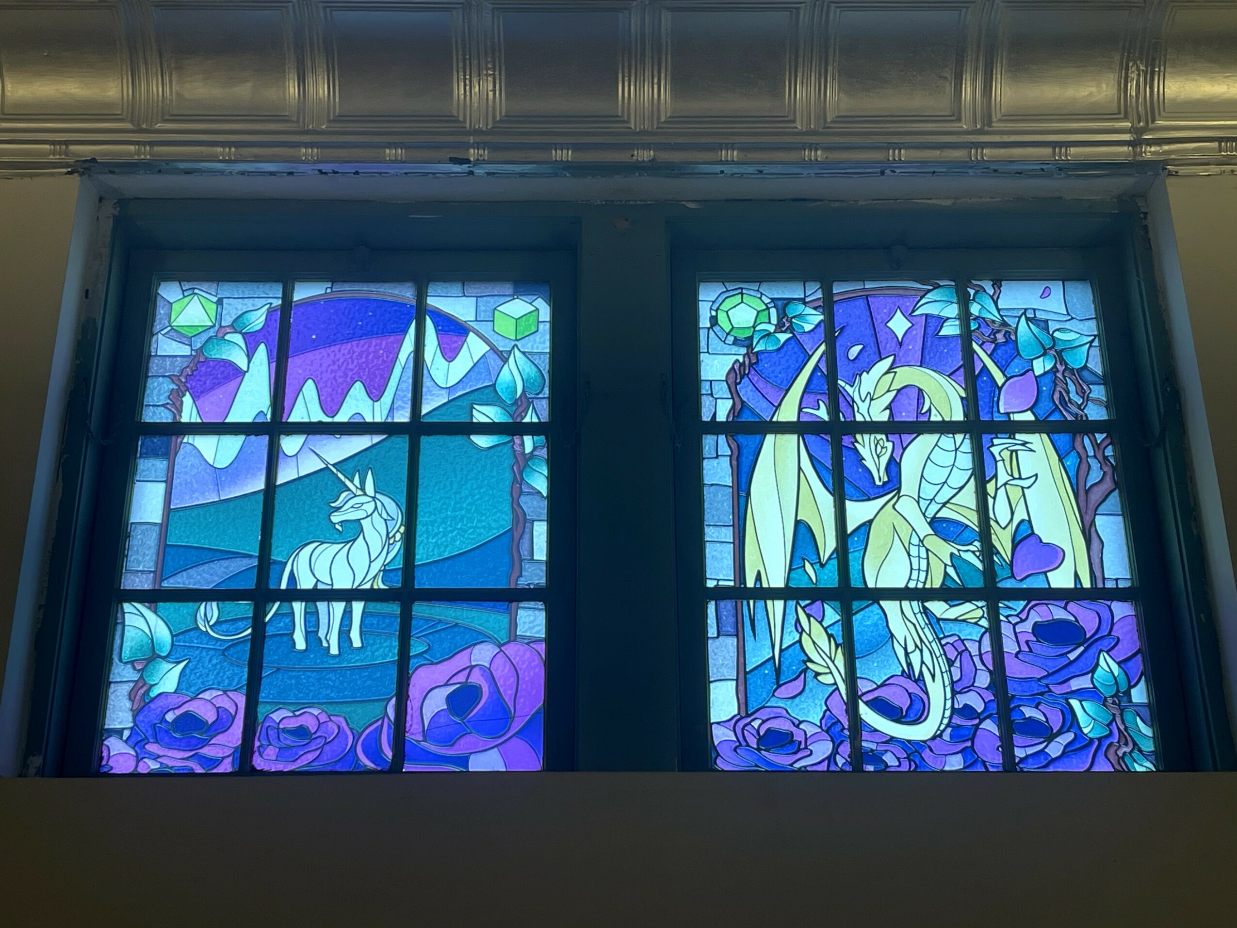 Stained glass window with unicorns, trees, and abstract shapes in blue, purple, and green colors.