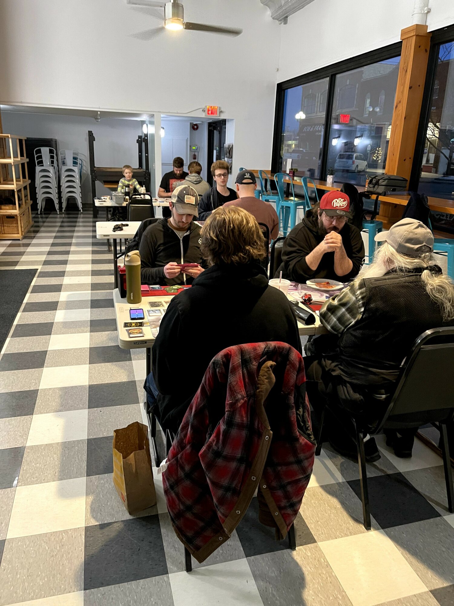 People sit at tables in a well-lit restaurant with large windows, eating and talking.