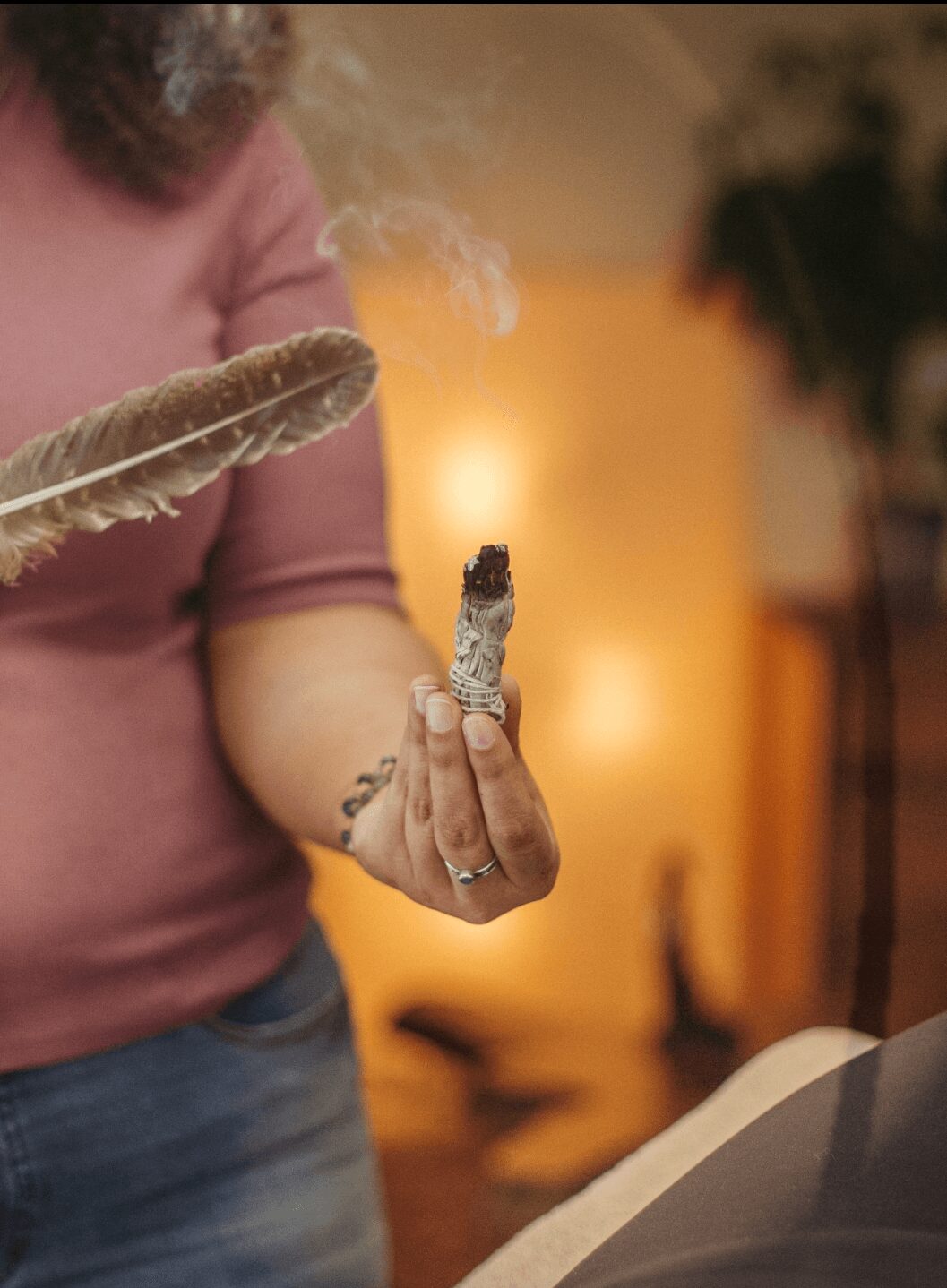 Person holding a smoldering stick with a glowing tip, indoors with warm lighting and blurred background.