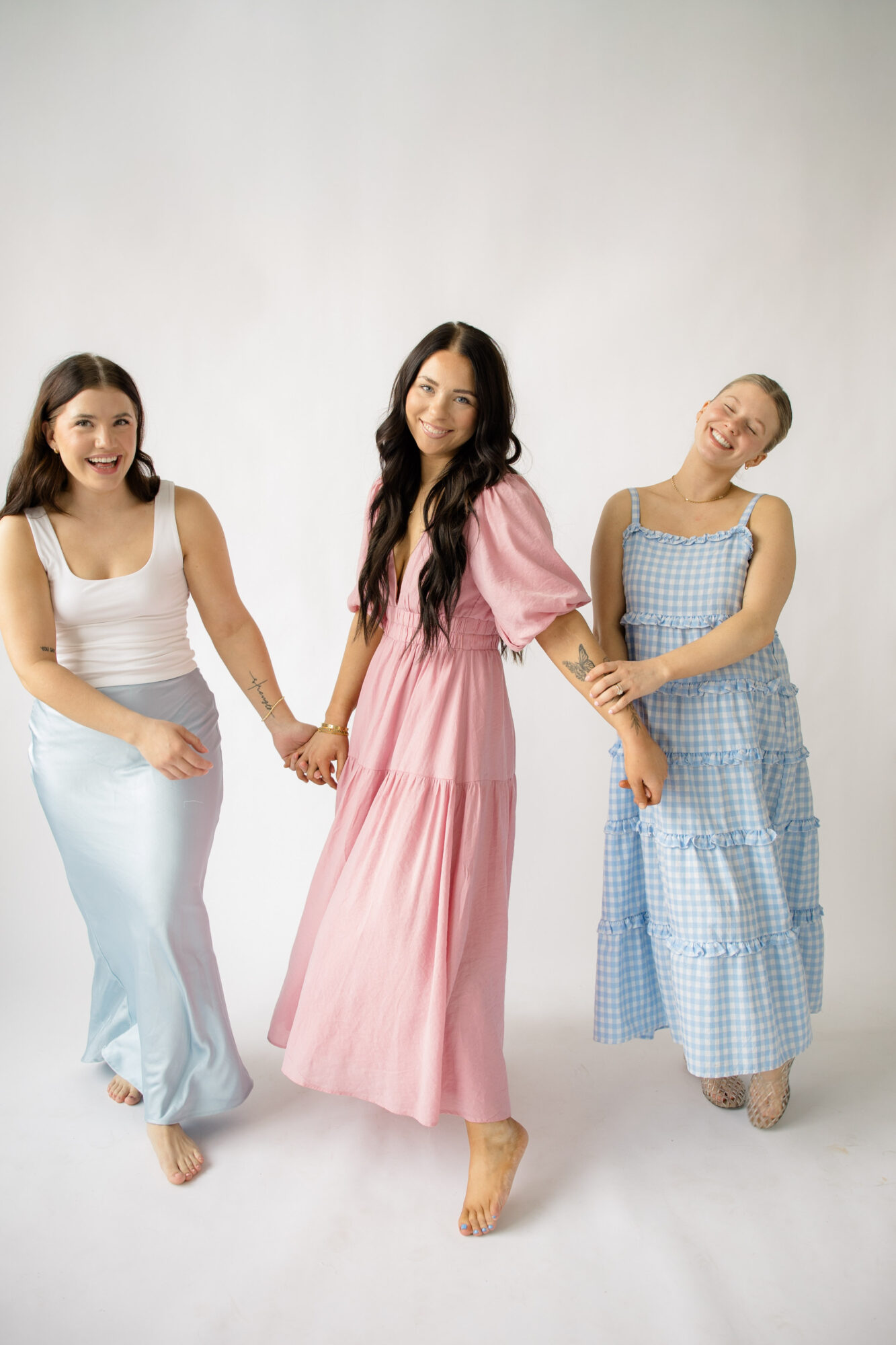 Three women holding hands and smiling, standing against a plain white background.