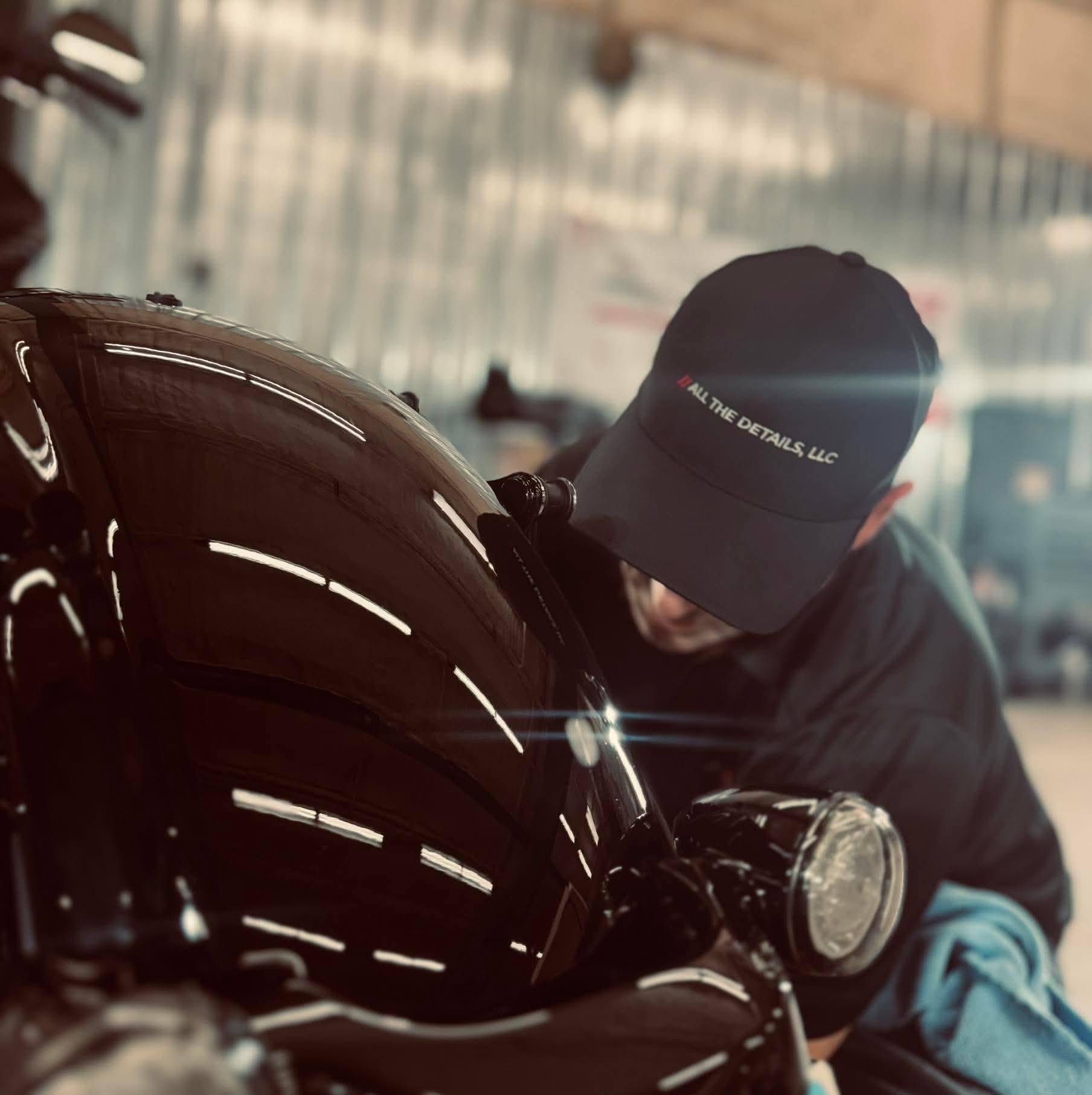 Person wearing a cap and dark clothing inspecting a motorcycle in an indoor setting.