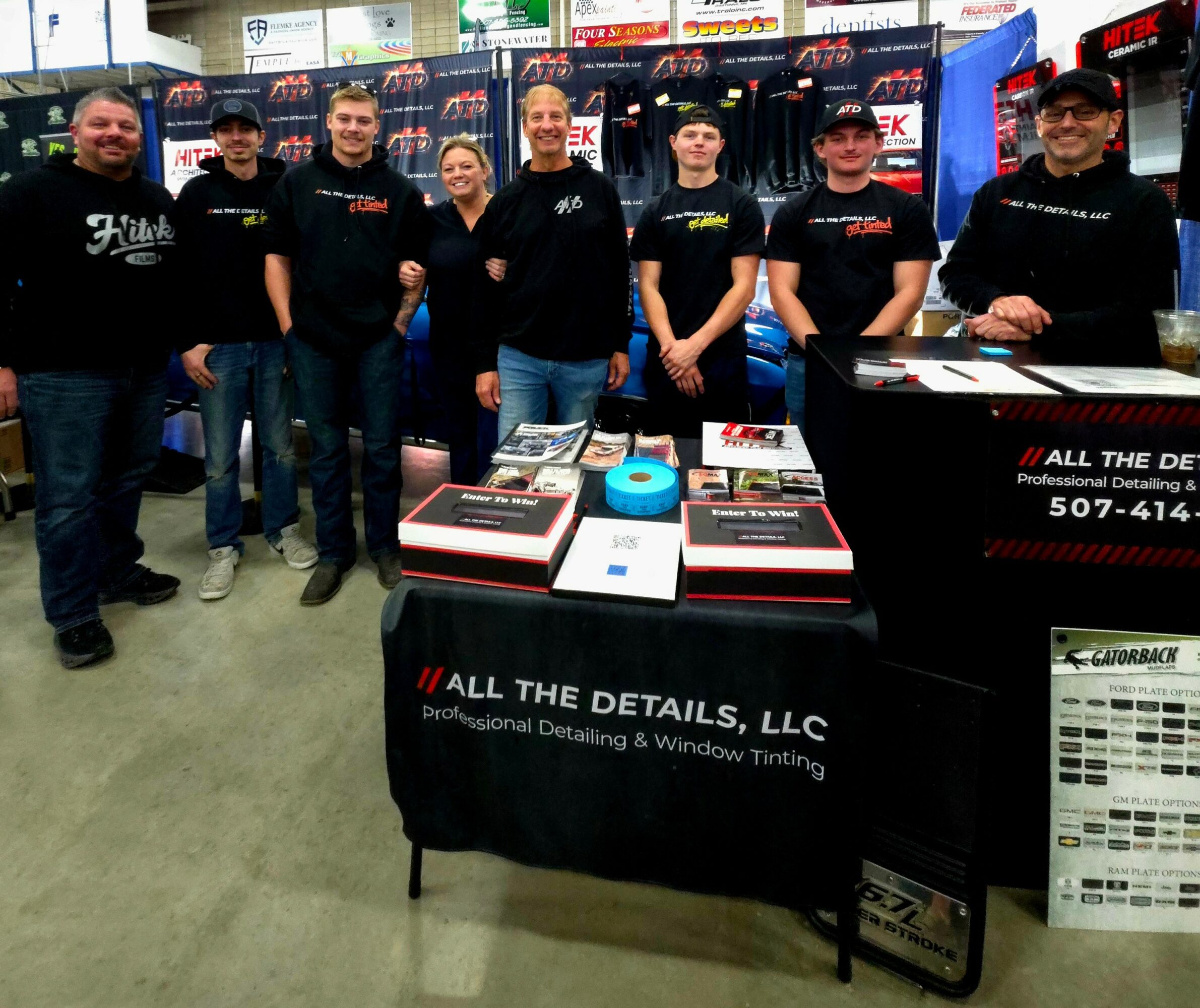 Group of seven people standing behind a table with detailing products at an indoor event.