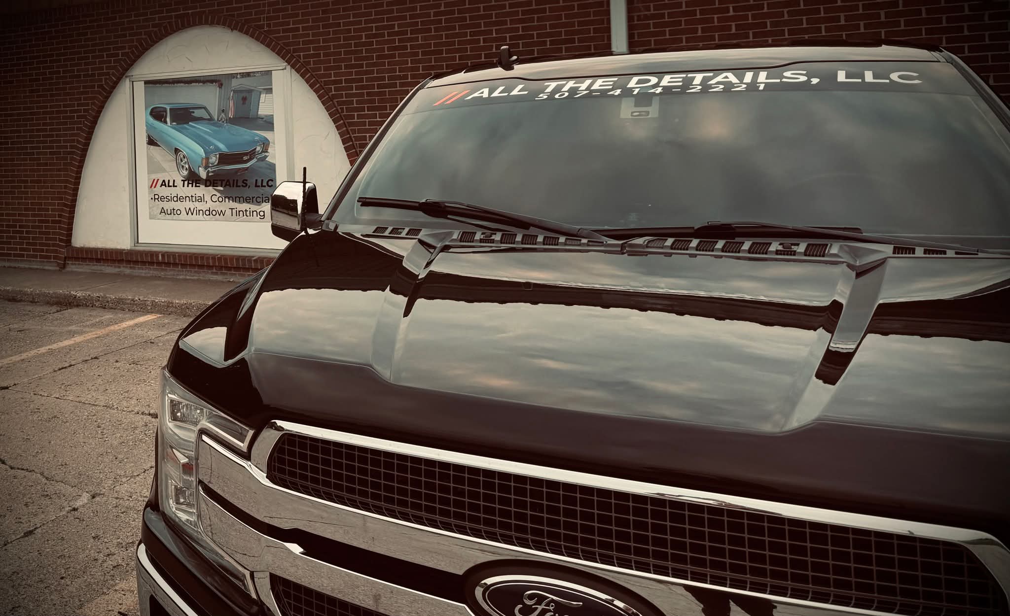 Black vehicle parked outdoors with a brick wall and a poster in the background.