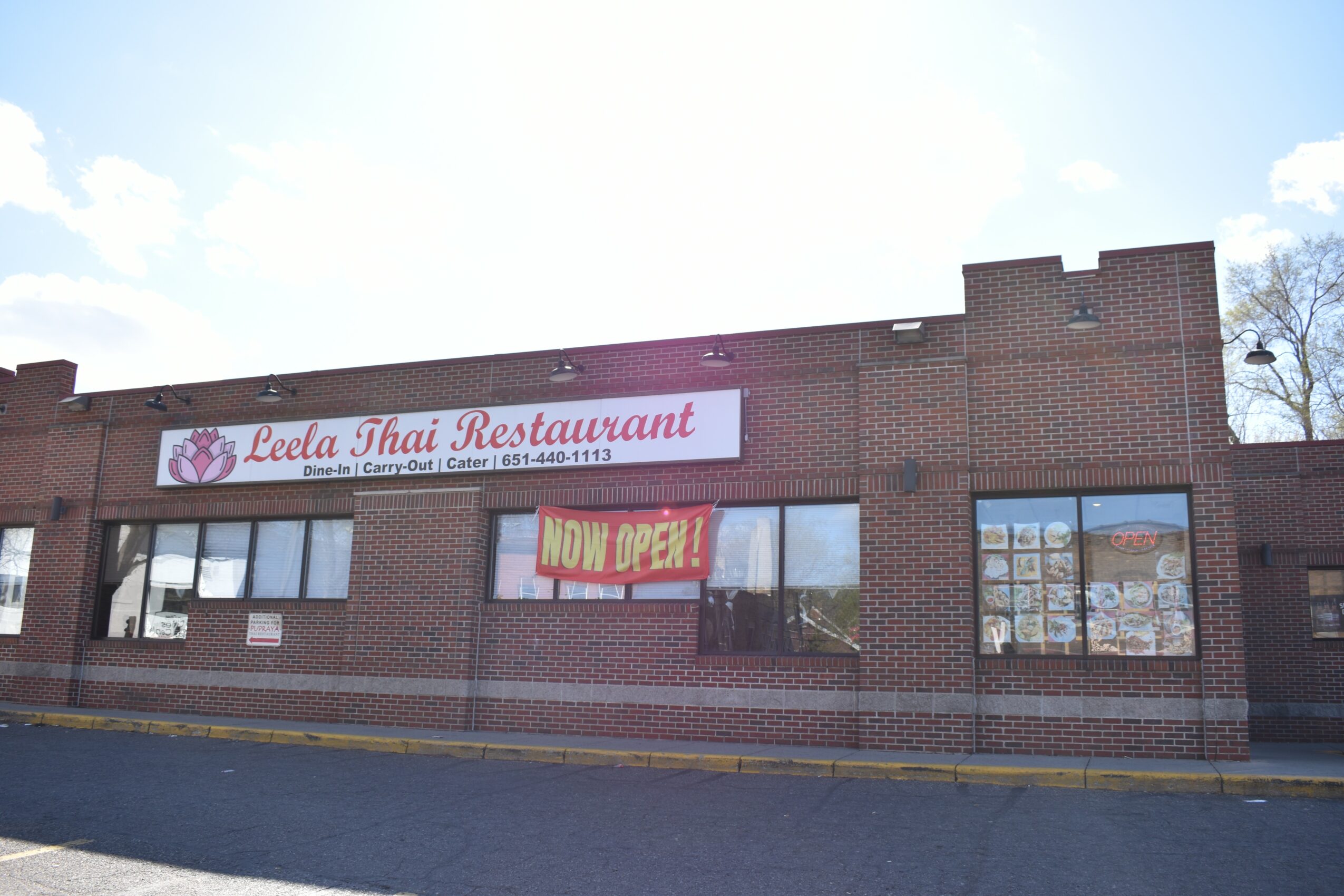 Brick building with signs for a Thai restaurant and an open sign, windows reflecting the street, and a clear sky.