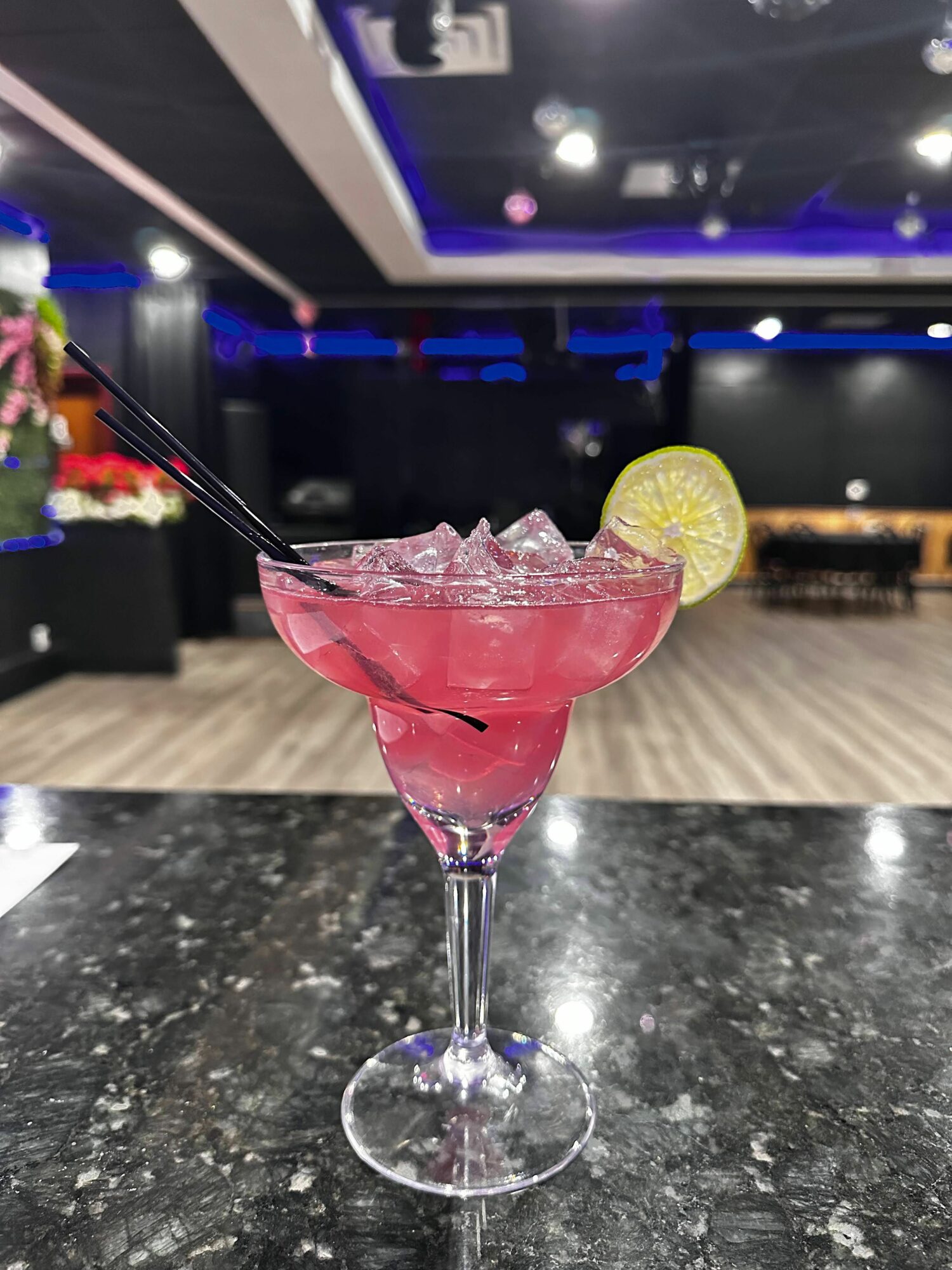 Pink cocktail with ice and lemon slice in a martini glass on a black marble surface.