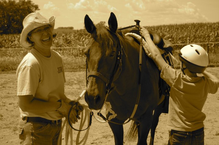 Two people with a horse outdoors, one person wearing a hat and the other wearing a helmet, in a field.