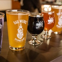 Four glasses of different colored beverages on a dark table, with a blurred background.