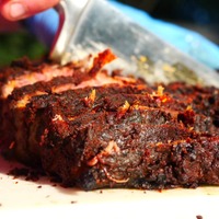 Sliced cooked meat with a dark, crispy exterior on a white surface.