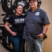 Two people standing side by side, smiling, in front of a black and white abstract wall art.