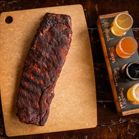 Barbecue ribs on a cutting board with sauce bottles nearby.