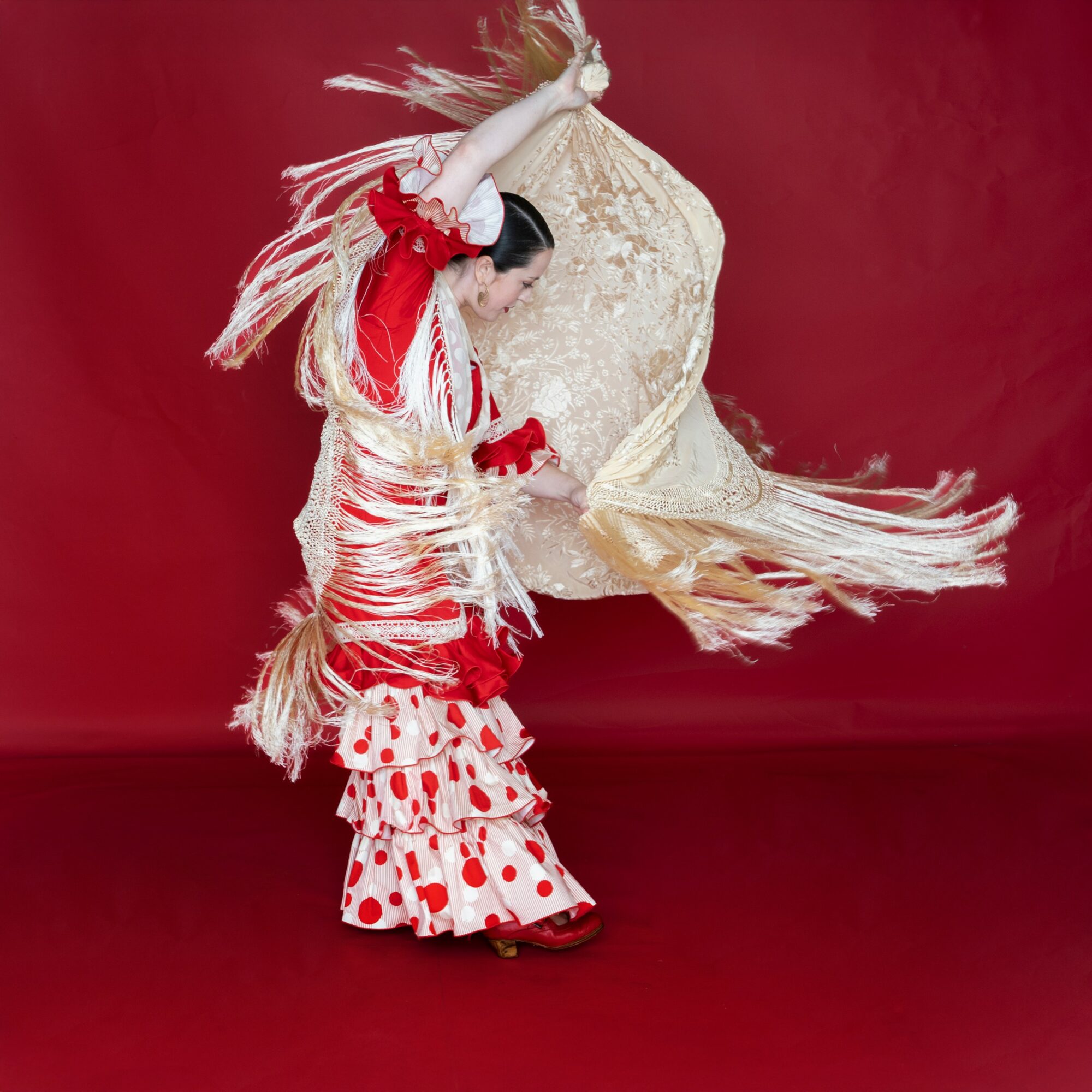 Person in traditional dress performing a dance with a large, decorated fan against a red background.