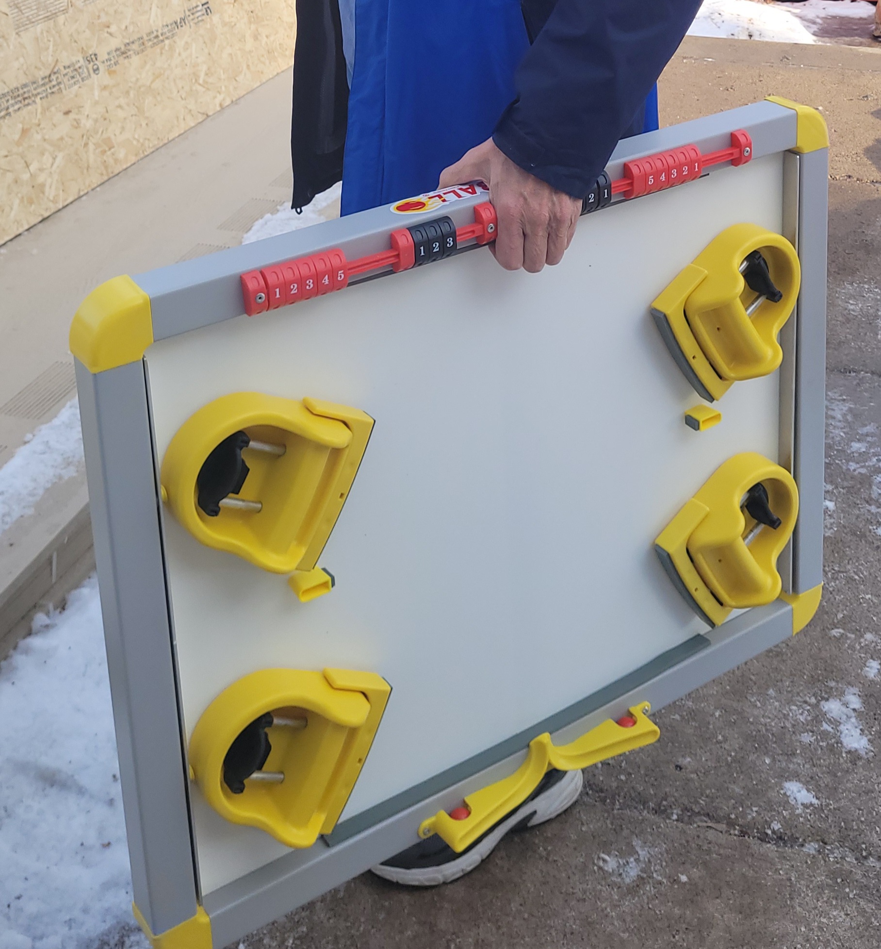 Person holding a whiteboard with yellow clamps and a red level, standing outdoors on a concrete surface.