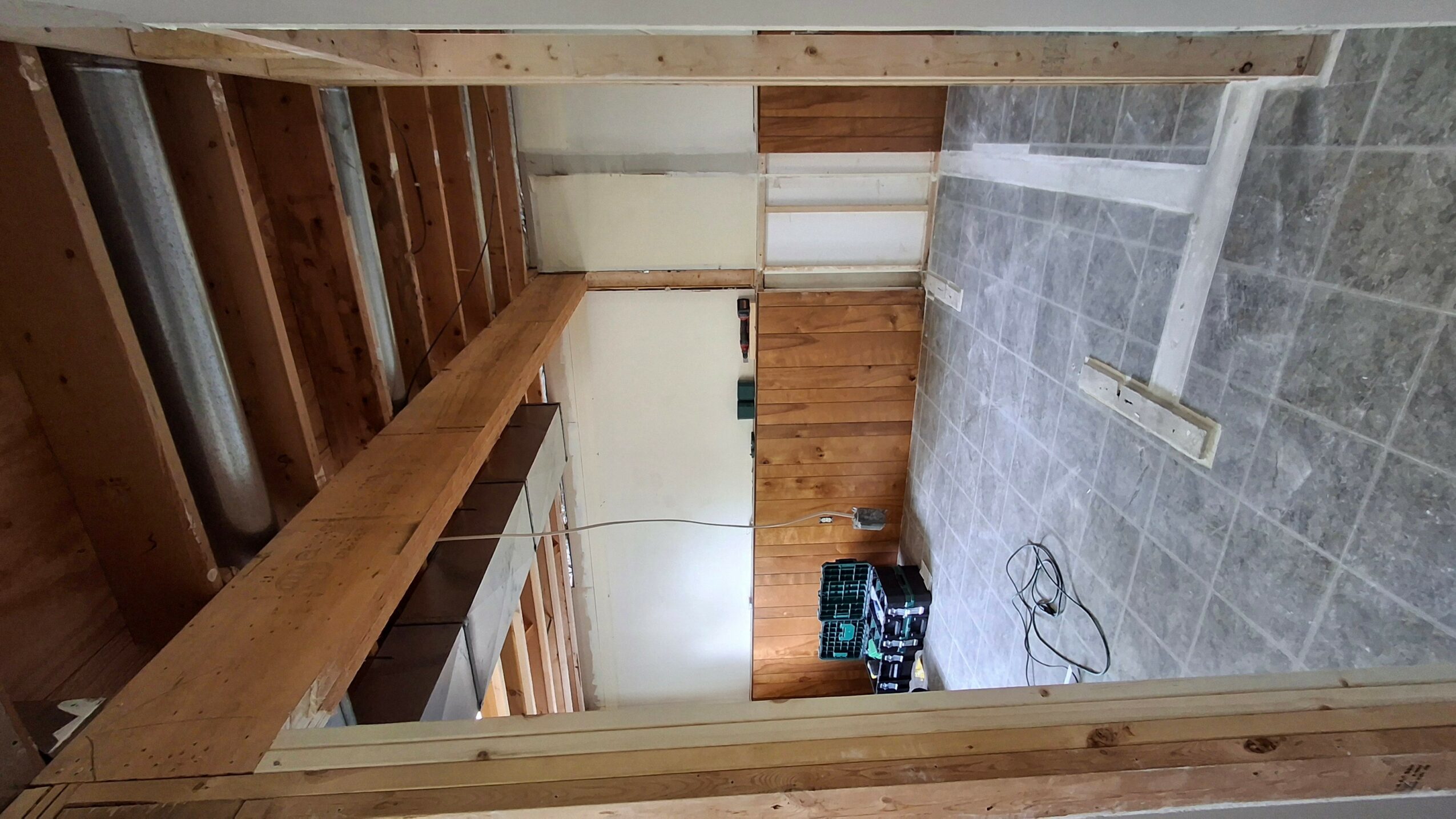 Room with wooden beams, tiled floor, and a partially finished wall. Tools and cables on the floor.