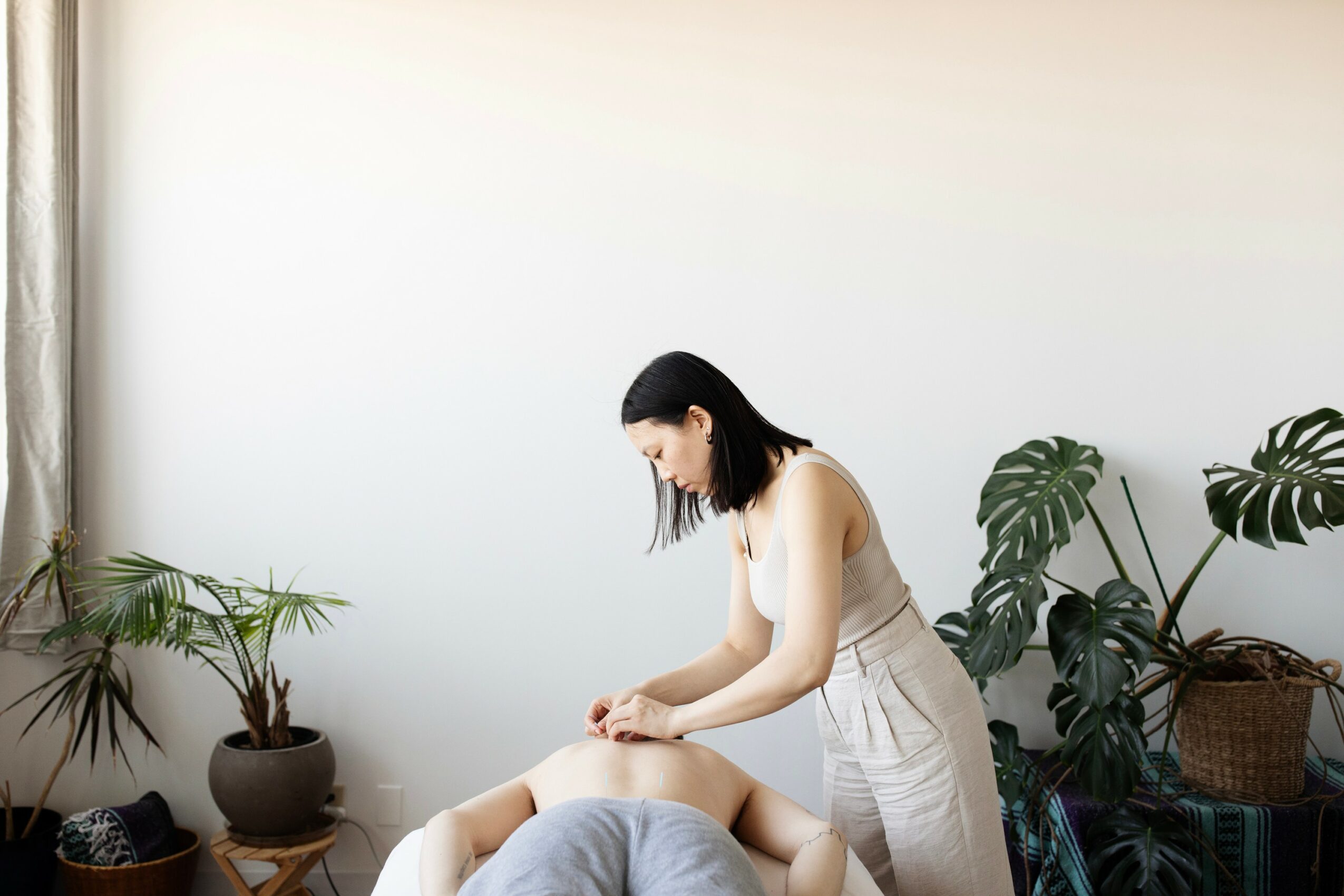 Woman in white dress receiving a massage in a room with plants and natural light.