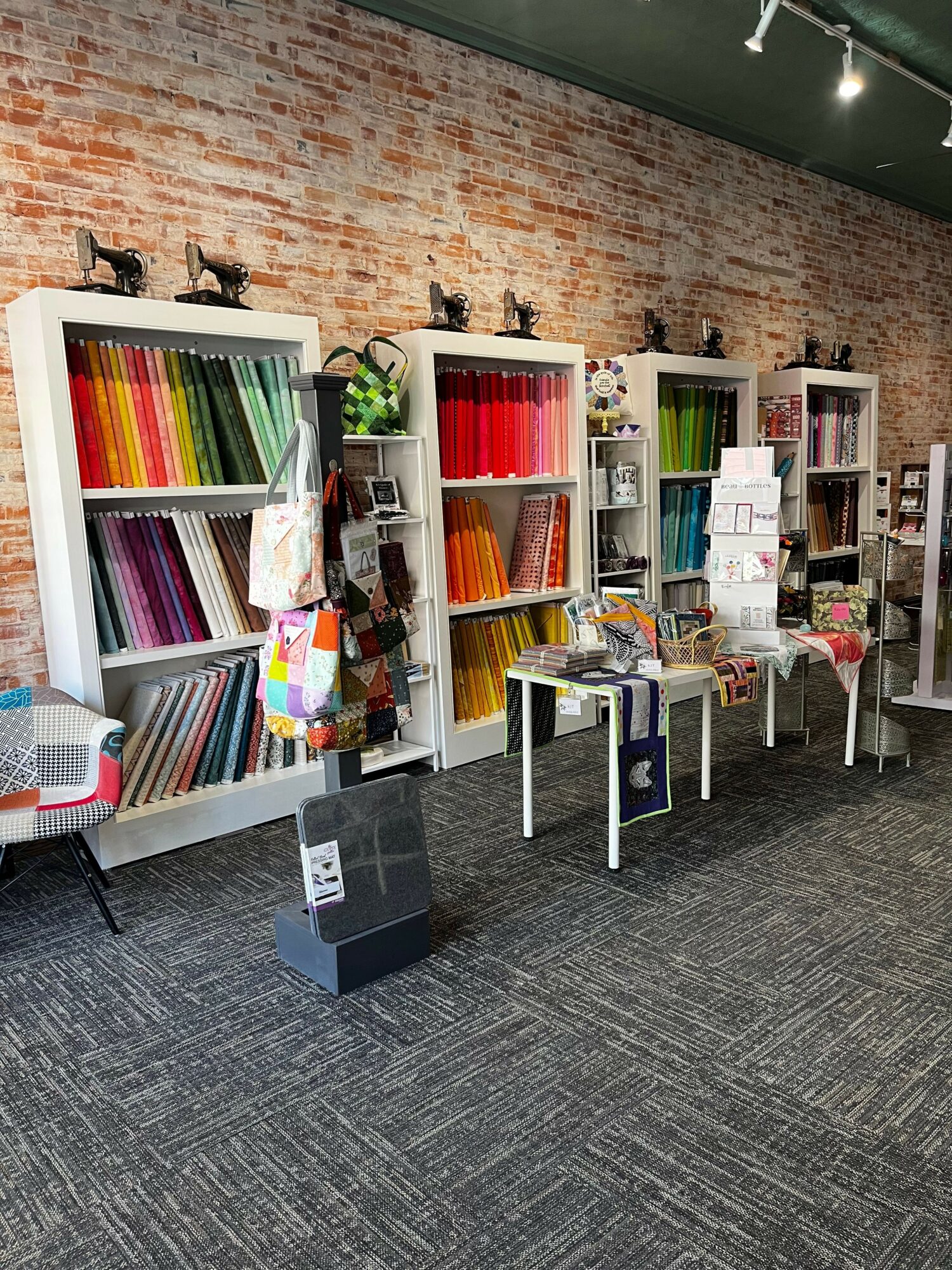 Bookshelves filled with colorful fabric samples and books in a room with brick wall and dark carpet.