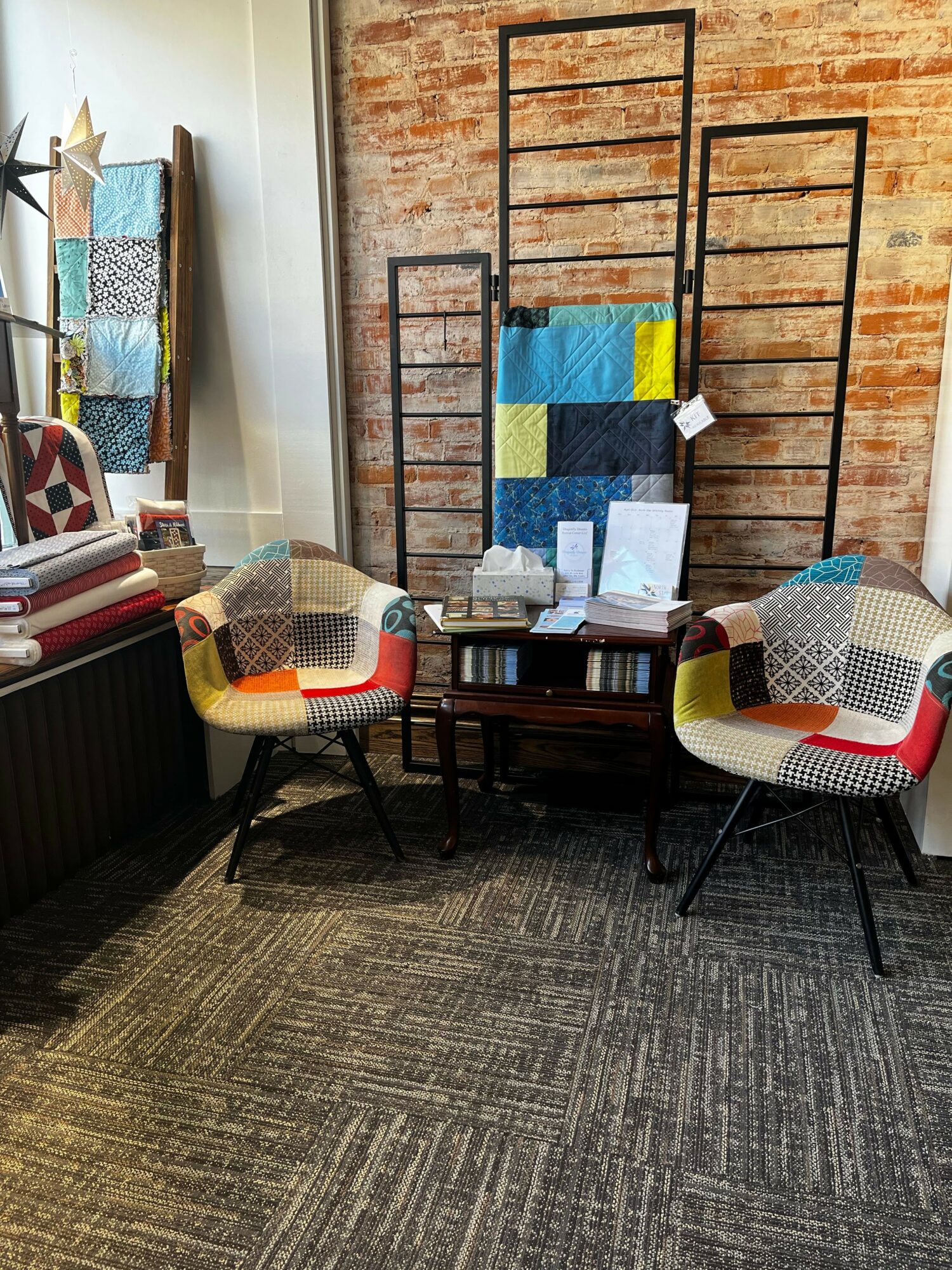 Interior space with a brick wall, a clothing rack, a patchwork armchair, a small table, and a patterned rug.