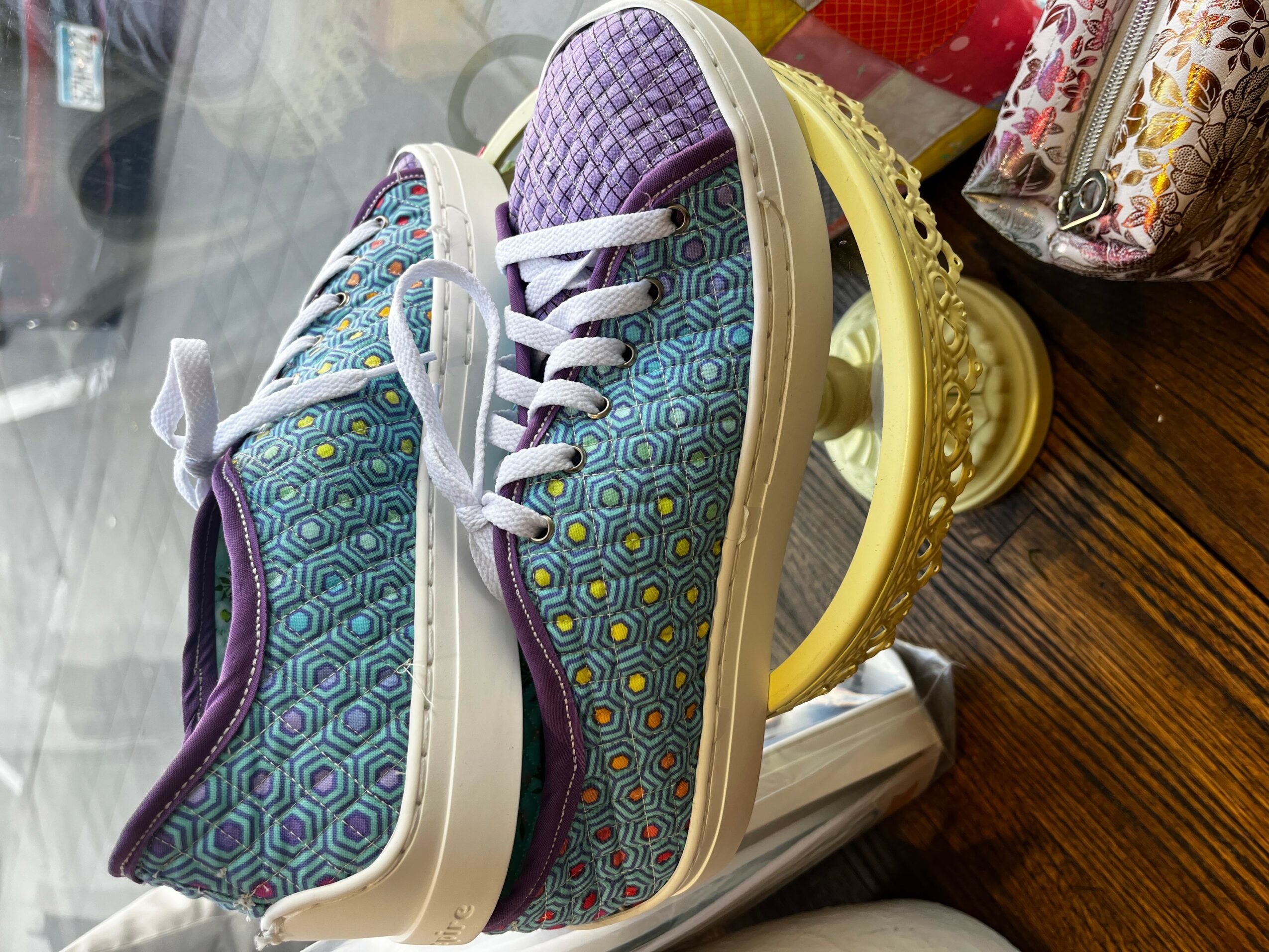 Pair of colorful sneakers with geometric pattern, placed on a yellow stand on a wooden surface.