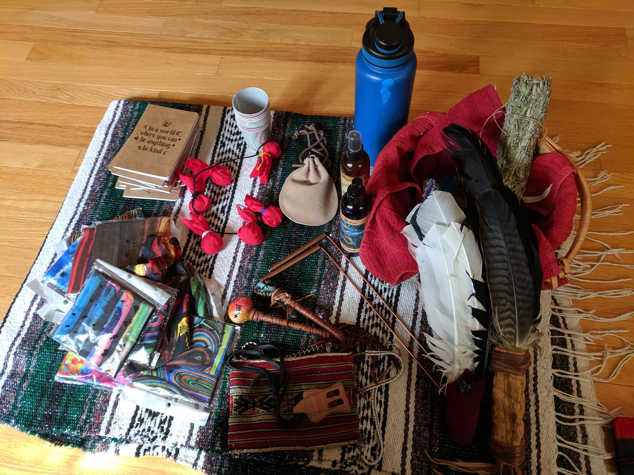 Various items on a table including notebooks, a water bottle, a red cloth, a black and white feather, and a wooden stick.