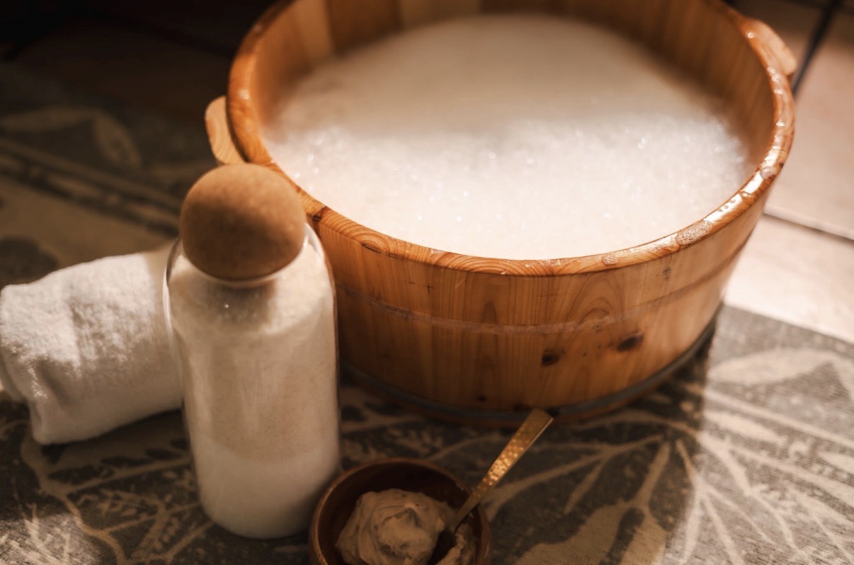 Bowl of soap suds, small towel, salt shaker, and spoon on patterned surface.