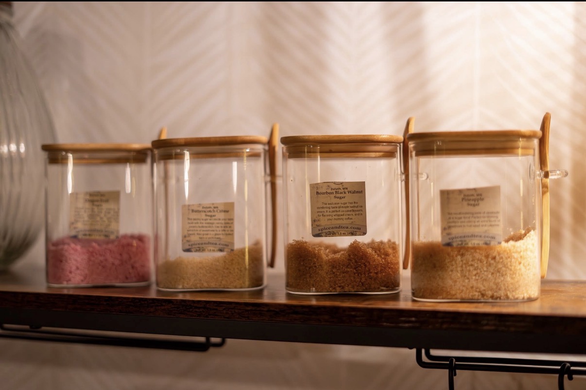 Four glass jars with wooden lids containing different colored powders on a wooden surface, with a blurred background.