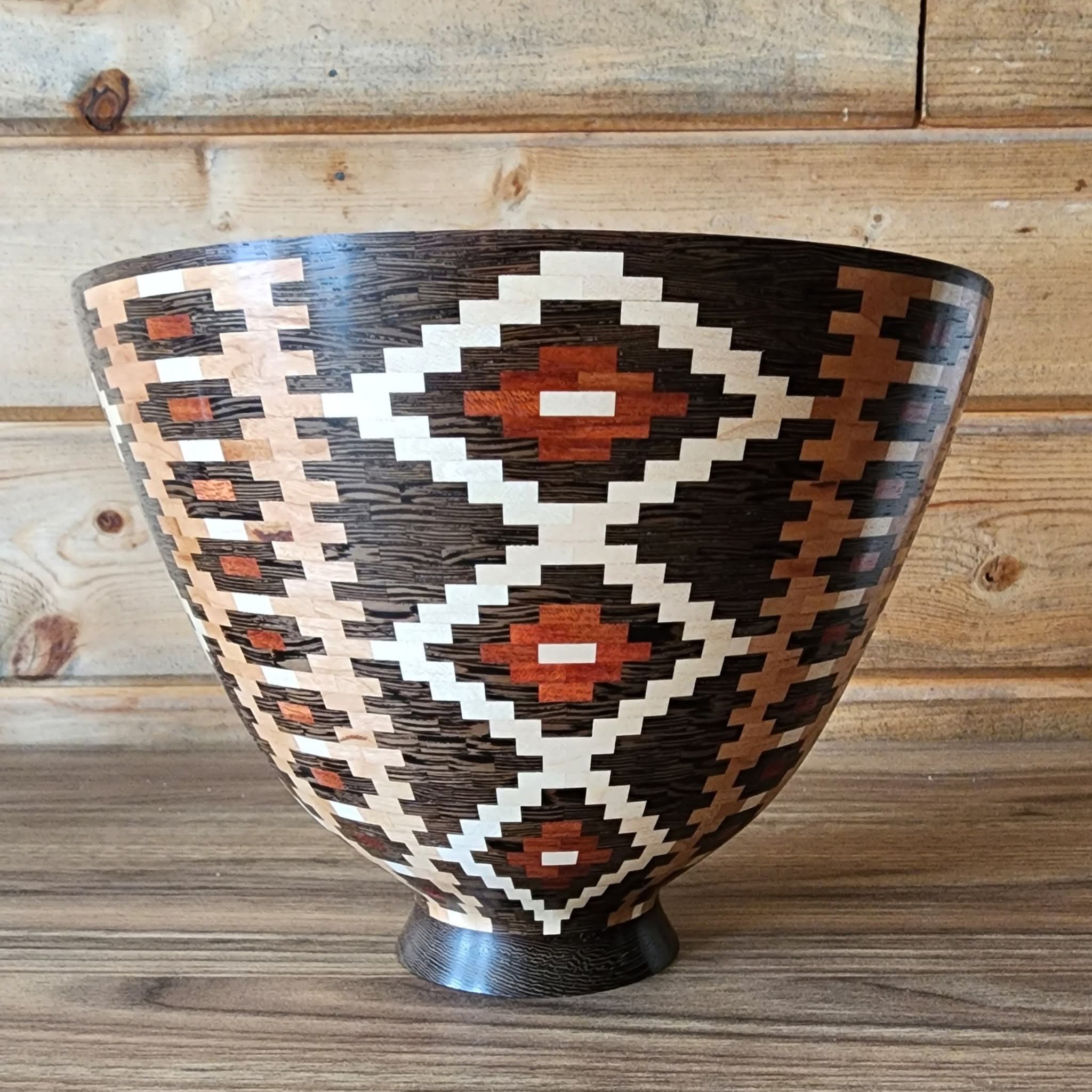 Decorative bowl with geometric pattern in black, white, and brown, placed on a wooden surface against a wooden background.