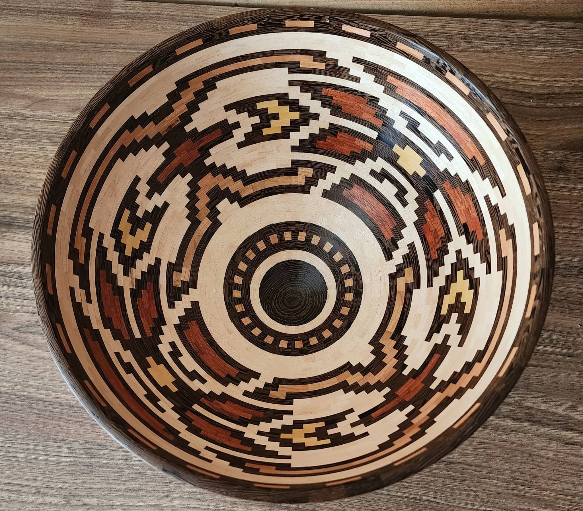 Decorative bowl with intricate geometric pattern in black, white, brown, and beige, placed on a wooden surface.