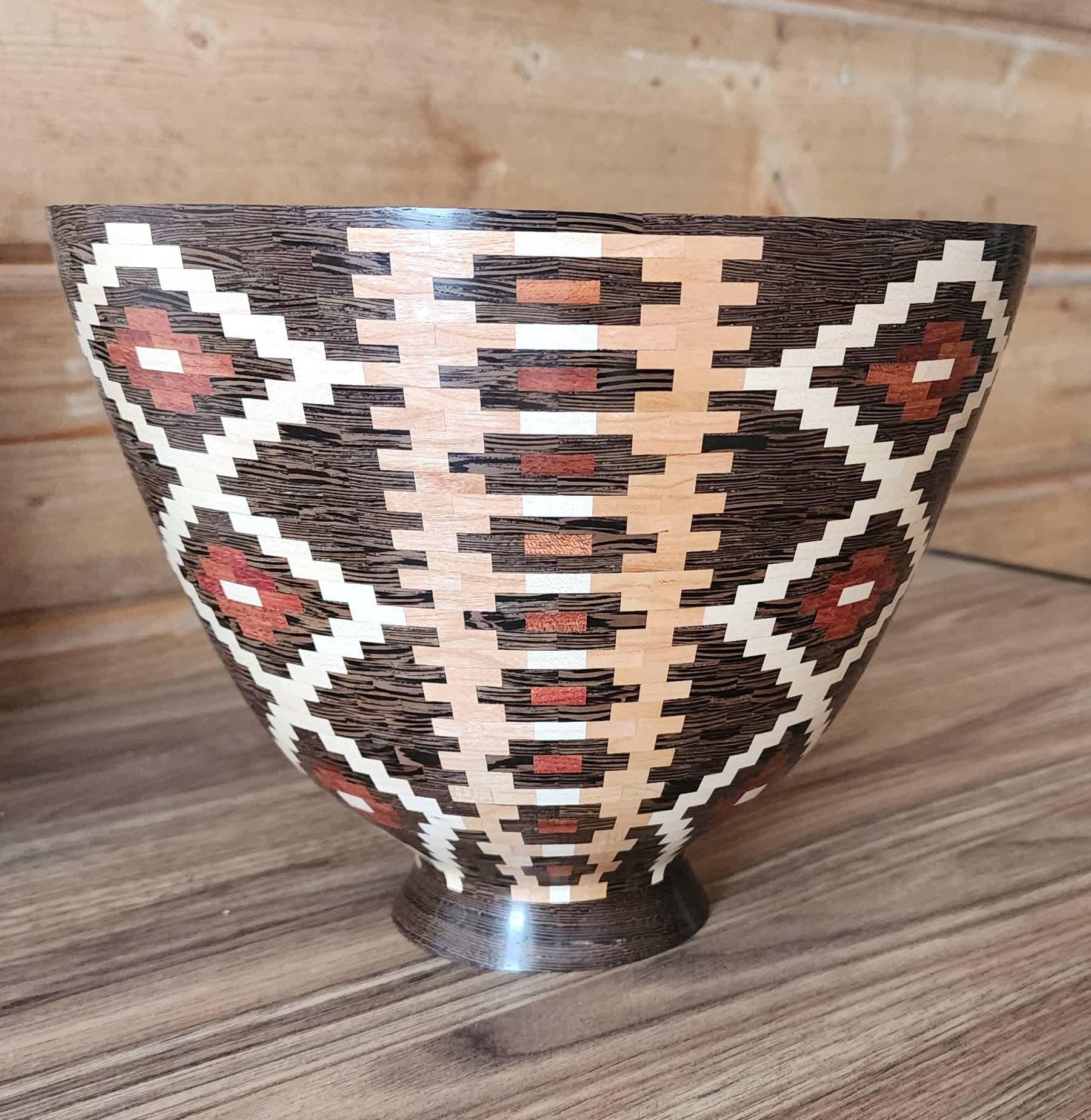 Decorative bowl with geometric patterns in black, white, red, and brown on a wooden surface.