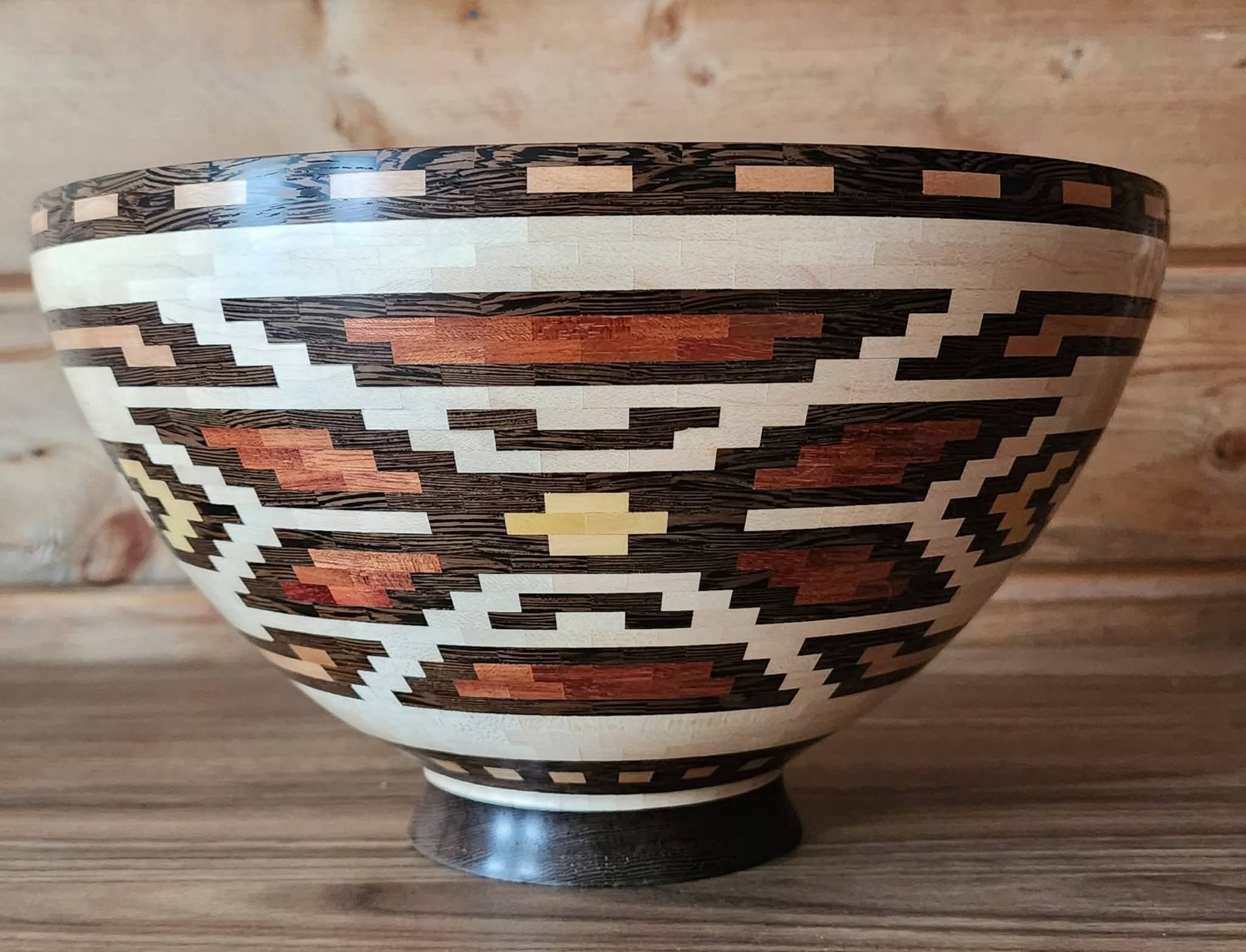 Decorative bowl with geometric patterns in black, white, red, and yellow, placed on a wooden surface.